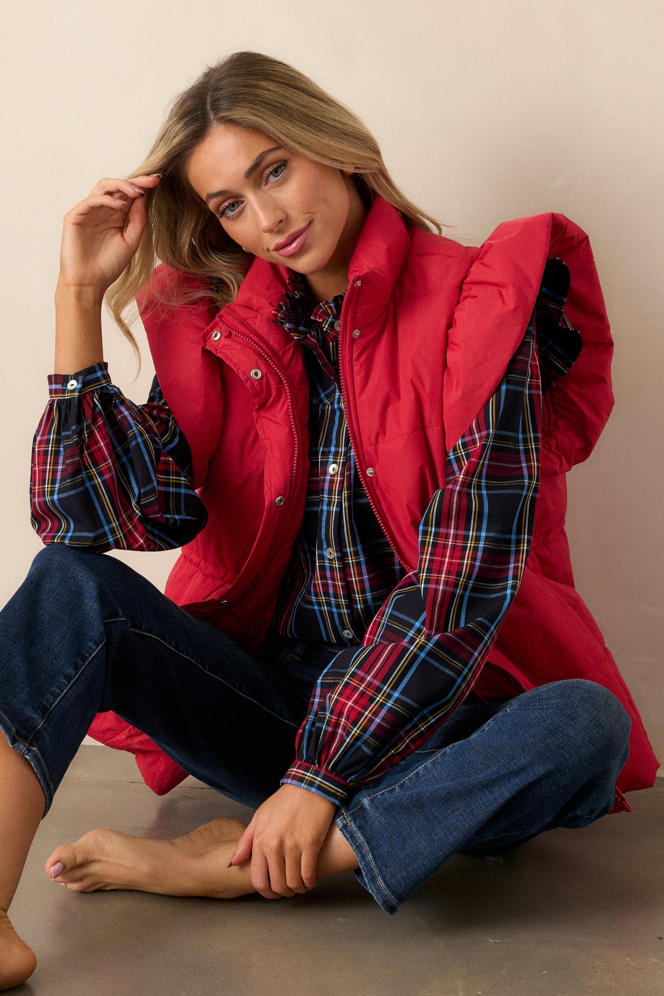 A red puffer vest with a high neckline and puffer line detailing, featuring a hidden snap button and zipper front, and a string cinch waist with silver hardware.