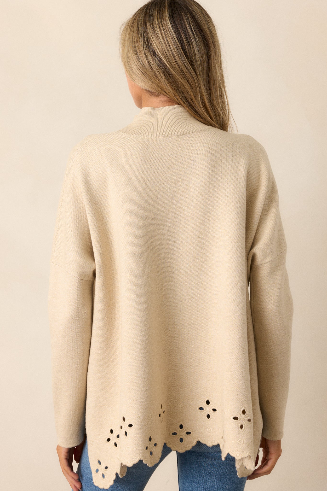 A back view of the sweater, showing the ribbed high neckline and the boxy, relaxed fit with the scalloped eyelet detail along the bottom hem.