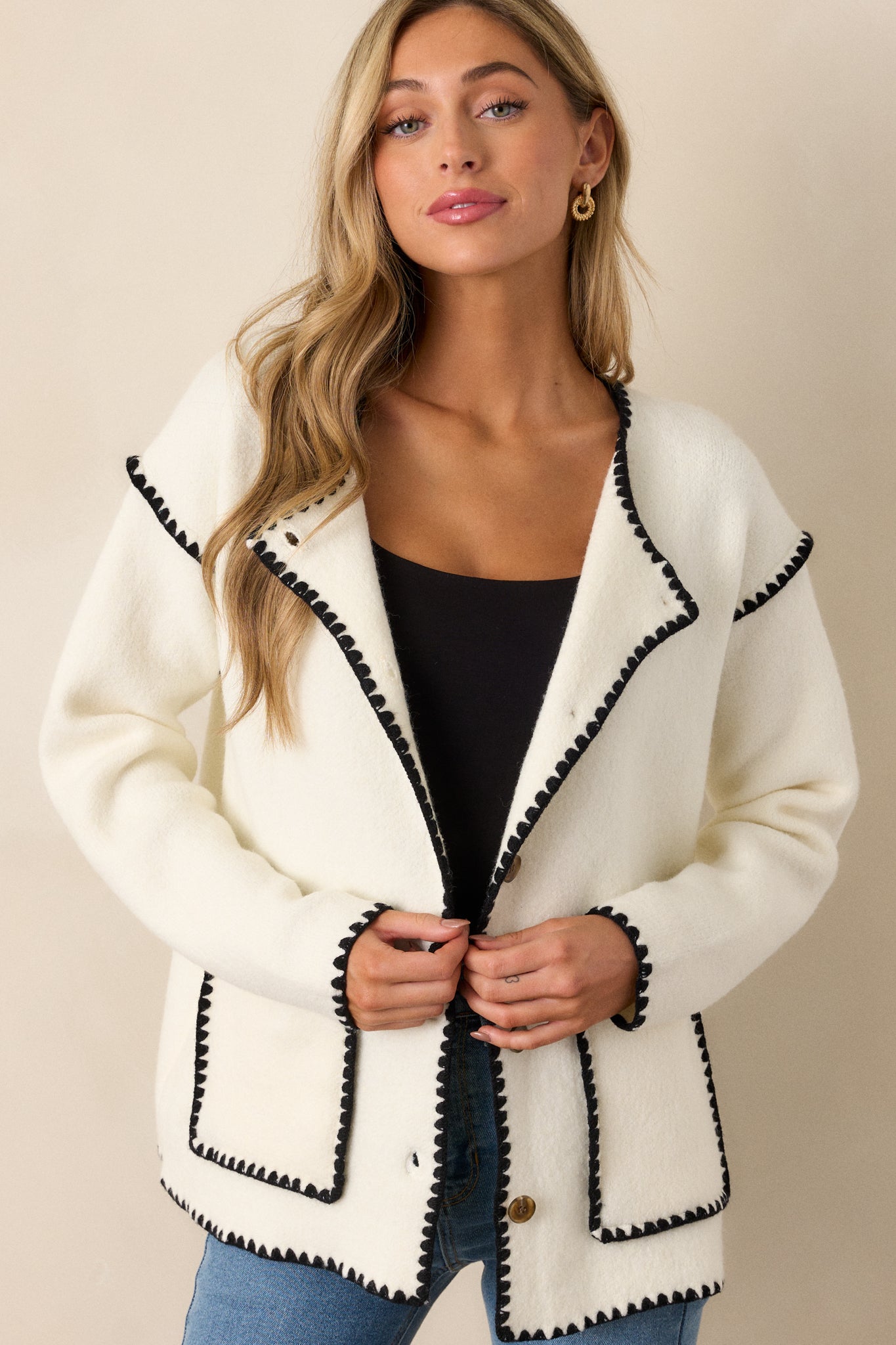 Front view of the white cardigan, showcasing the rounded neckline, brown tortoise buttons, and black blanket stitch trim along the edges.