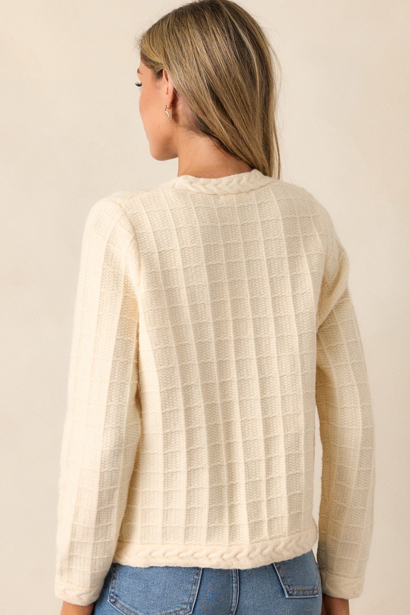 Rear view of the ivory cardigan, highlighting the full cable knit grid design across the back and the clean lines of the braided knit hems.