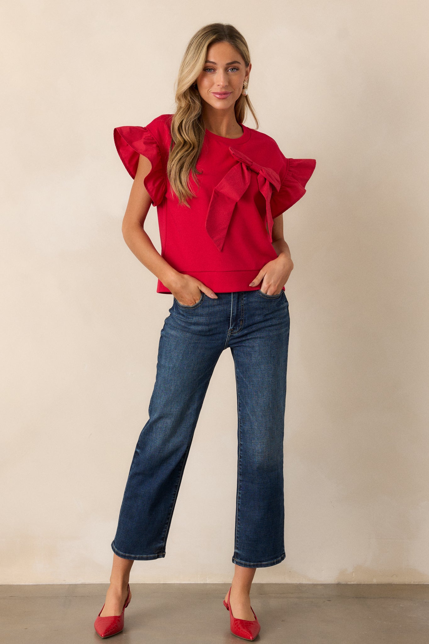 A red top with a crew neckline, featuring ruffle short sleeves and a bow accent on the front.