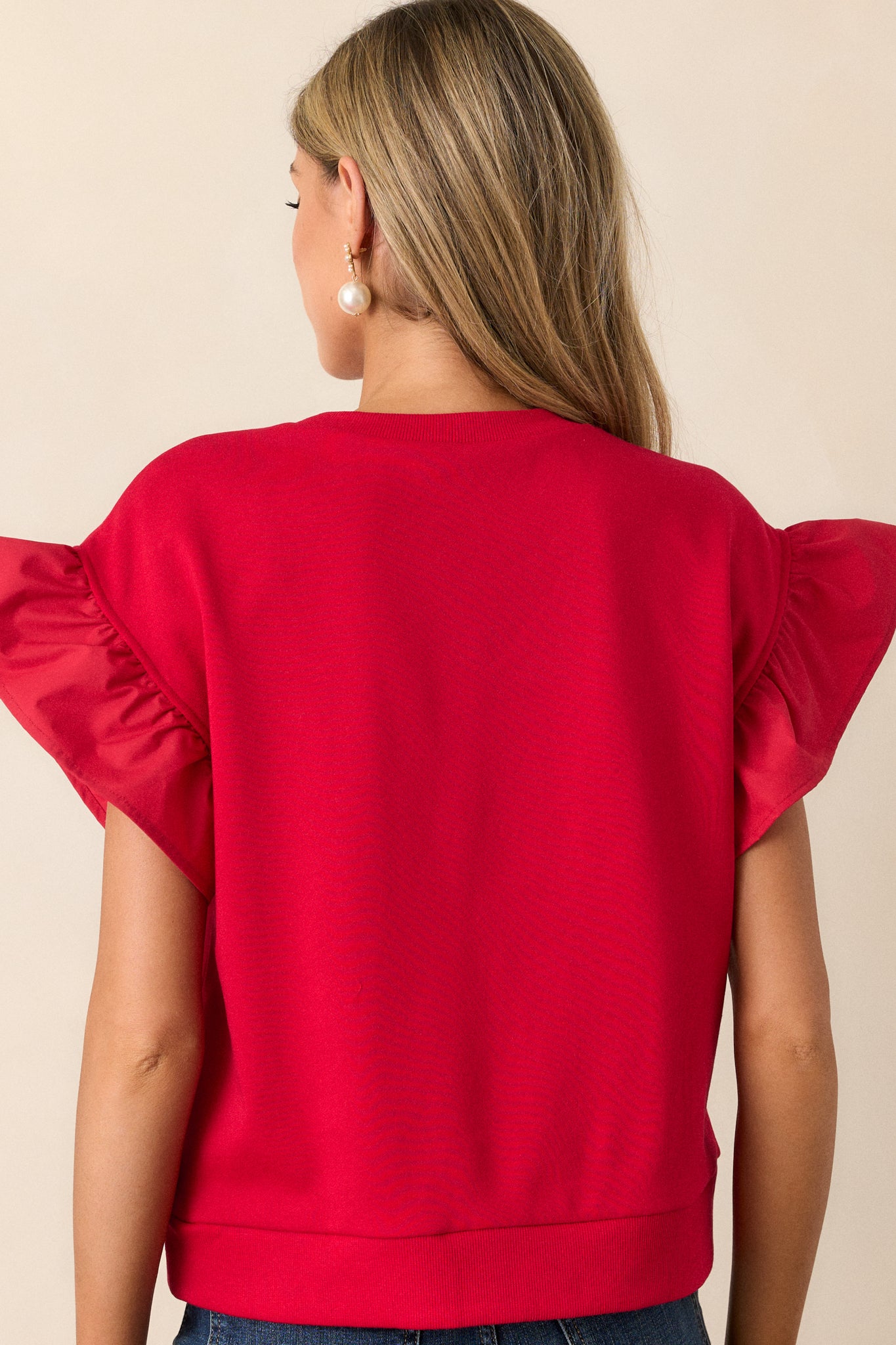 The back of the red top, featuring a simple, clean design with a smooth fit and visible ruffle sleeve details.