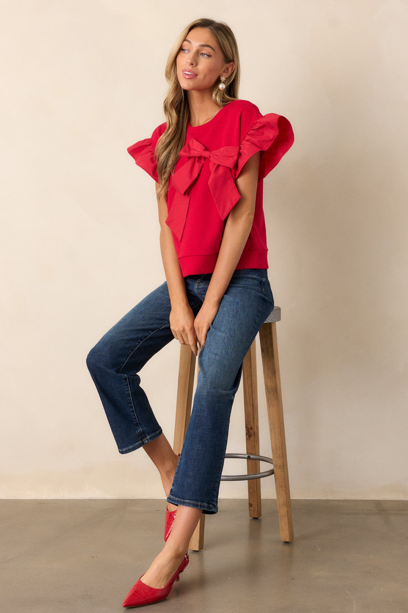 A red short-sleeve top with ruffle details, a crew neckline, and a ribbed hem, with a bow accent at the front.