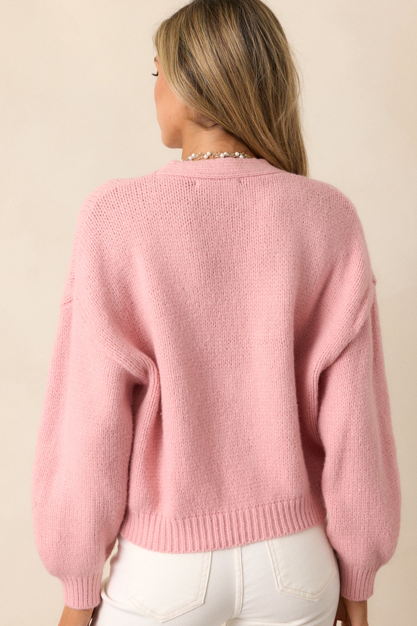 The back view of the pink knit cardigan, highlighting the cropped fit and dropped shoulders, creating a chic and modern look.