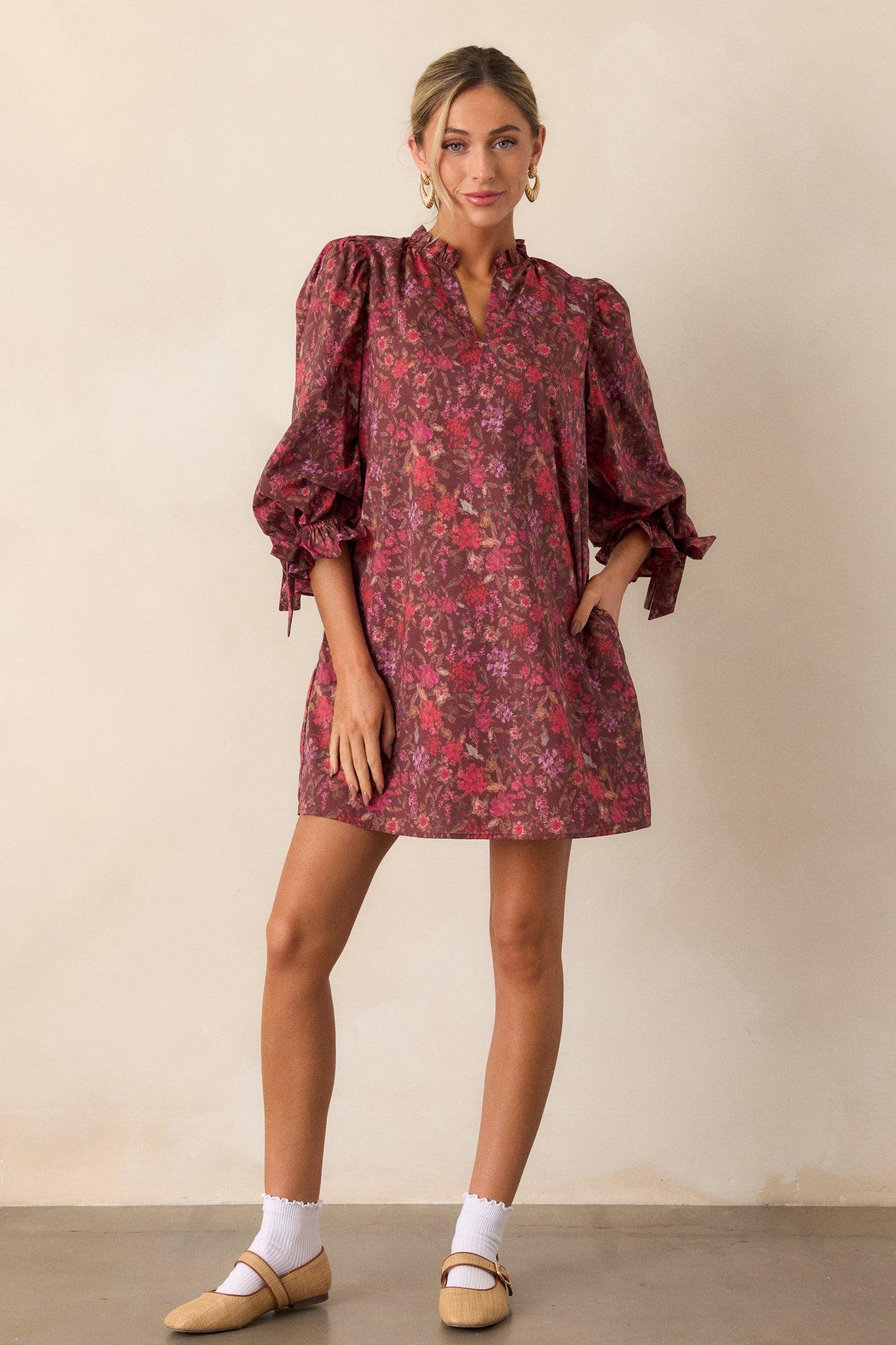 Burgundy dress with a floral pattern, showcasing a boxy silhouette, v-neckline, and functional hip pockets, complemented by ruffle detailing on the sleeves.