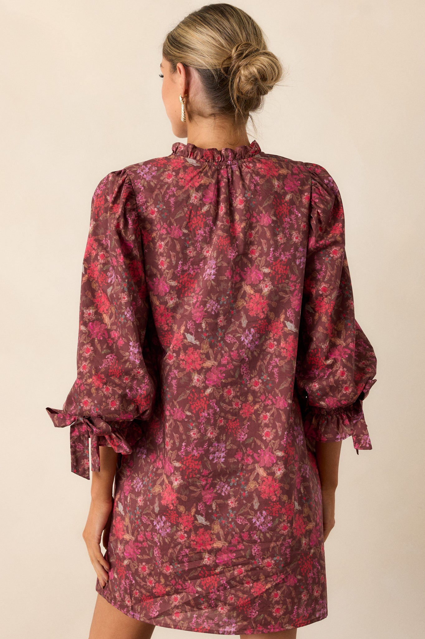 The back of the burgundy mini dress featuring a boxy fit, 3/4 length puff sleeves, and a seamless design that complements the floral pattern.