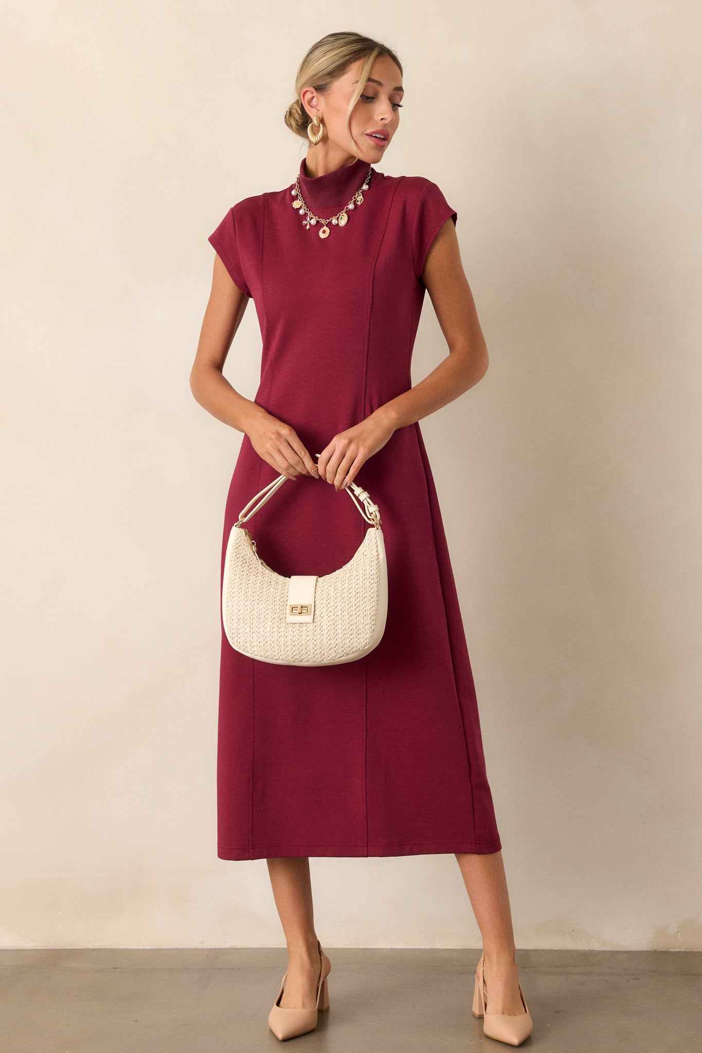 A burgundy midi dress featuring a sleek sheath silhouette with a mock turtleneck, showcasing its elegant and minimalistic design.