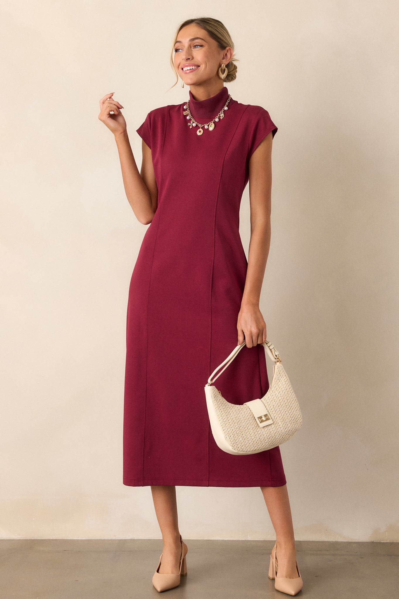 A angled view of the burgundy midi dress, emphasizing the smooth lines of the sheath silhouette and the sophisticated mock turtleneck style.