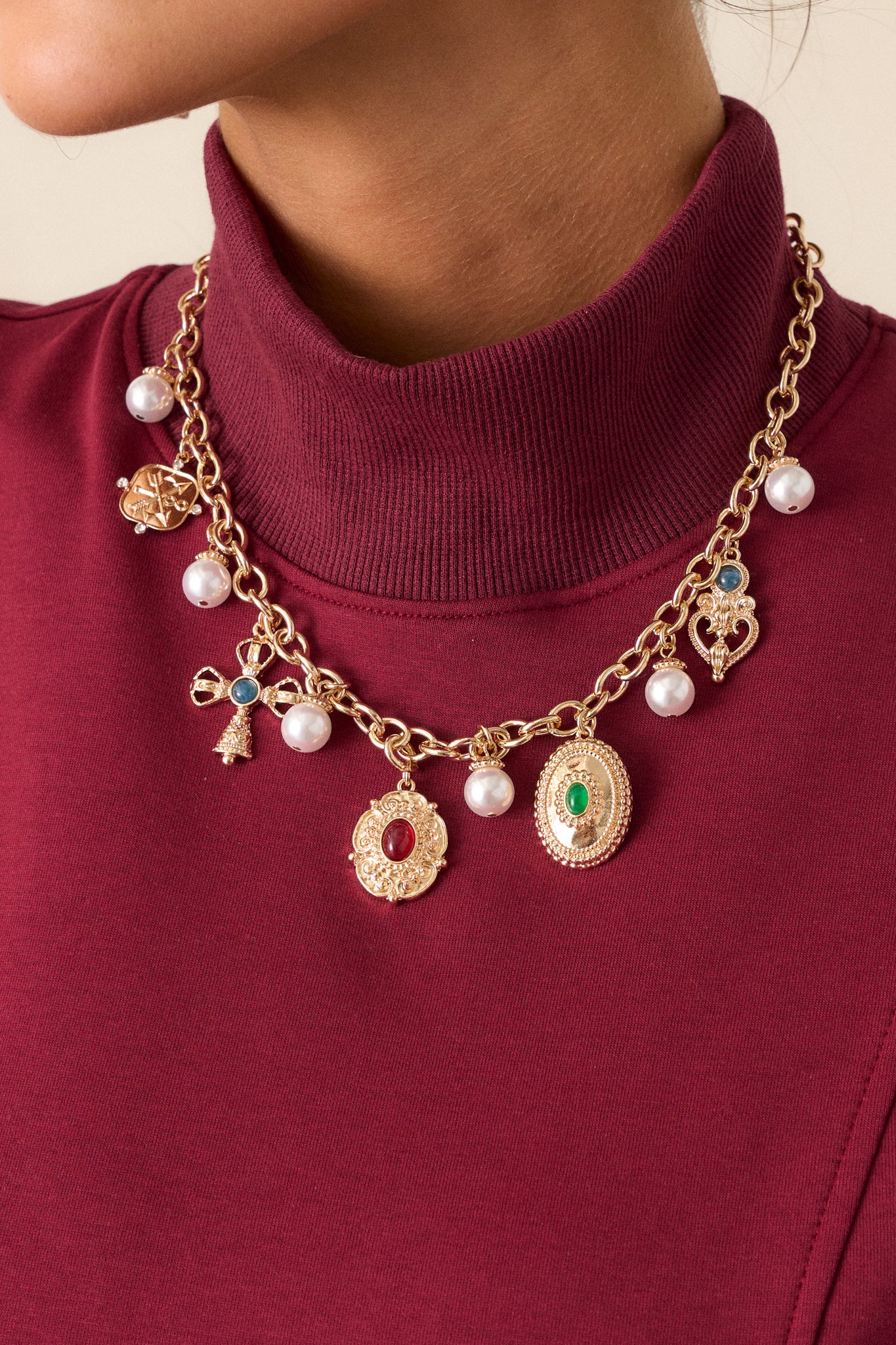 Close-up of the gold necklace, focusing on the intricate details of the charms and pendants, as well as the lustrous finish of the ivory faux pearls throughout.






