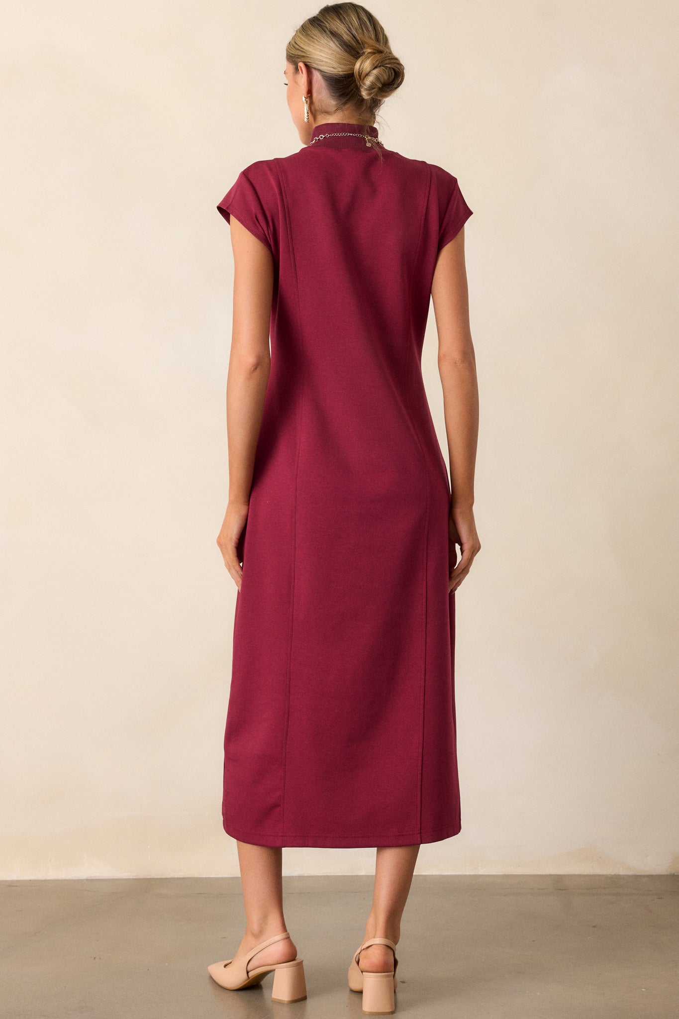 The back view of the burgundy midi dress, highlighting the mock turtleneck and the streamlined design that defines its elegant shape.