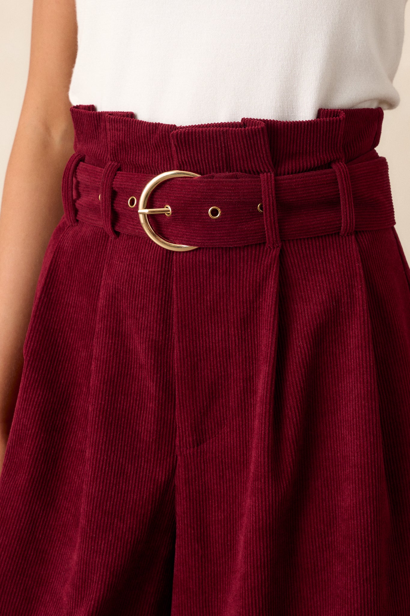 Close-up of the burgundy pants focusing on the paper bag style waistline, the adjustable belt, and the zipper closure.