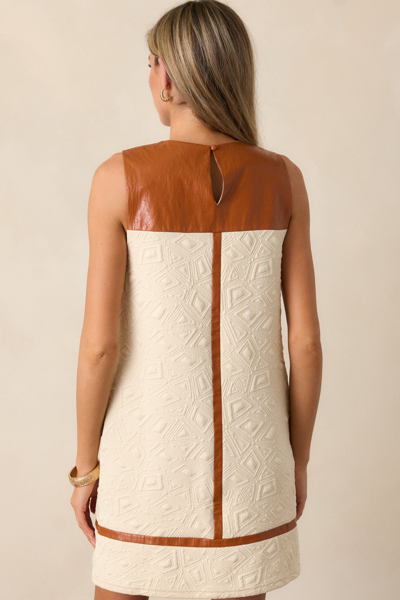 Back view of the ivory mini dress, showcasing the sleeveless design and quilted fabric with faux leather yolk detail across the shoulders.