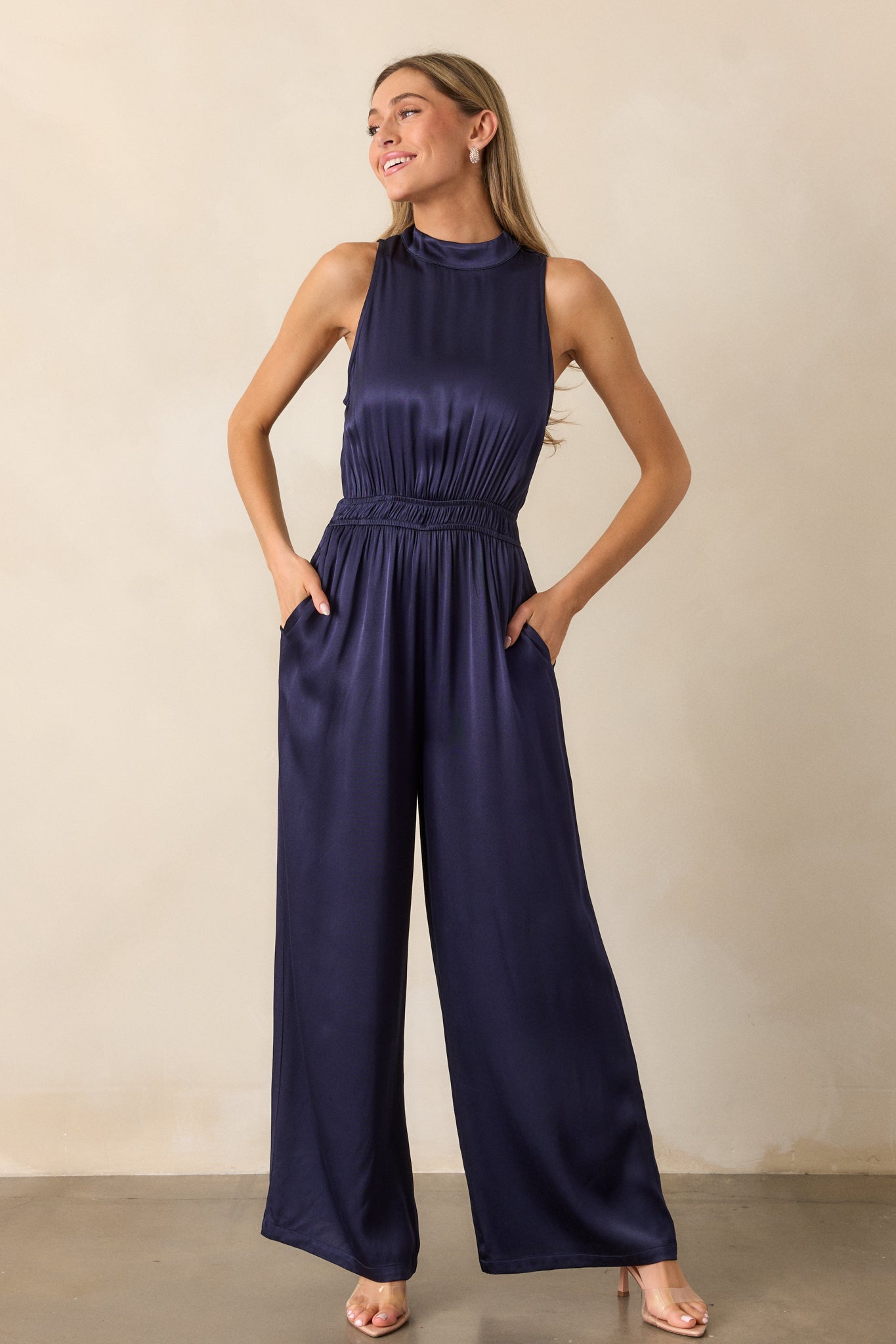 Full length view of the jumpsuit, highlighting the flowing pant legs, the cinched waist, and the button neck clasp at the high neckline.