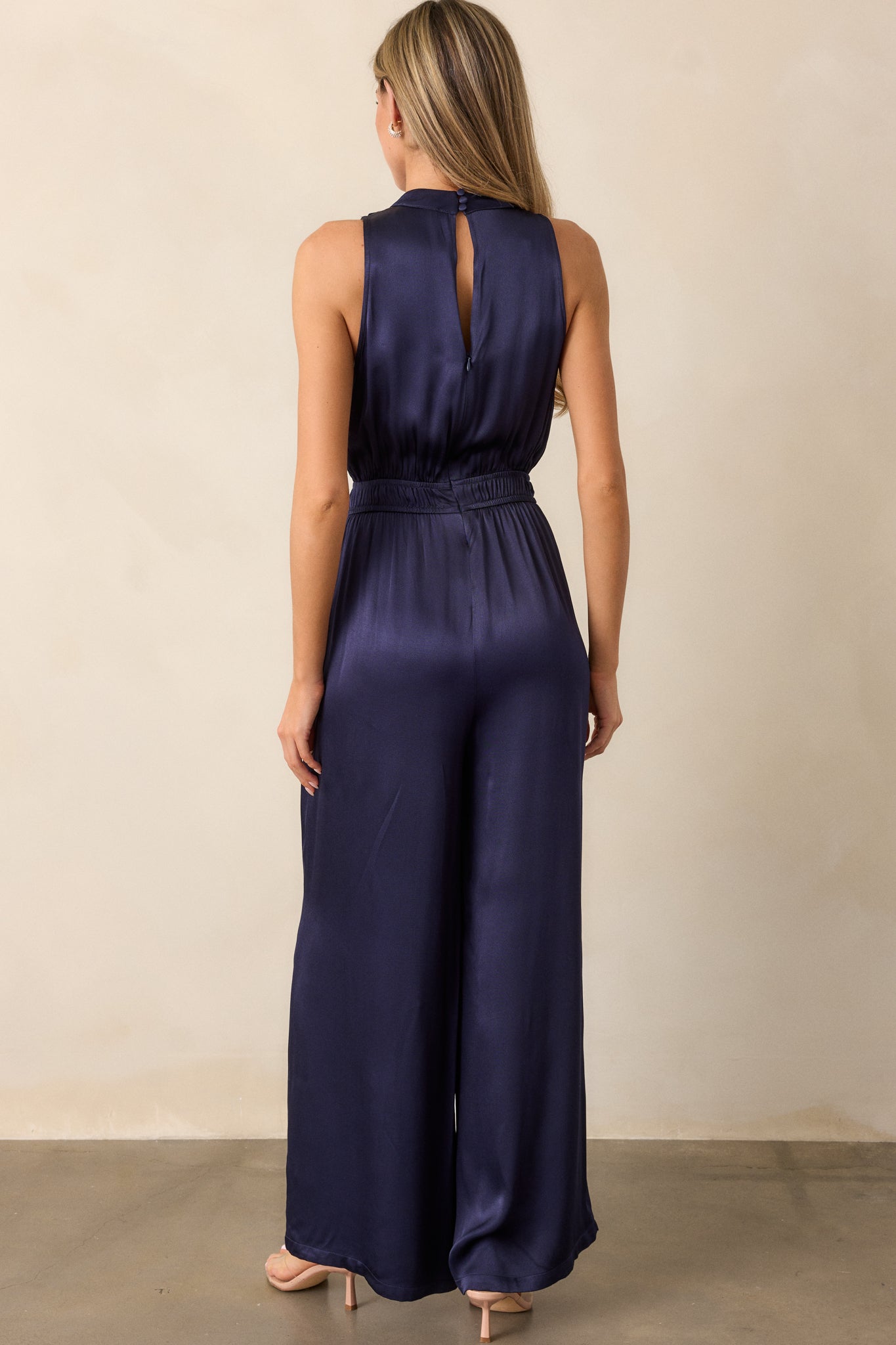 Full back view of the jumpsuit, focusing on the discrete back zipper, the smooth flow of the pant legs, and the subtle curve created by the cinched waist.