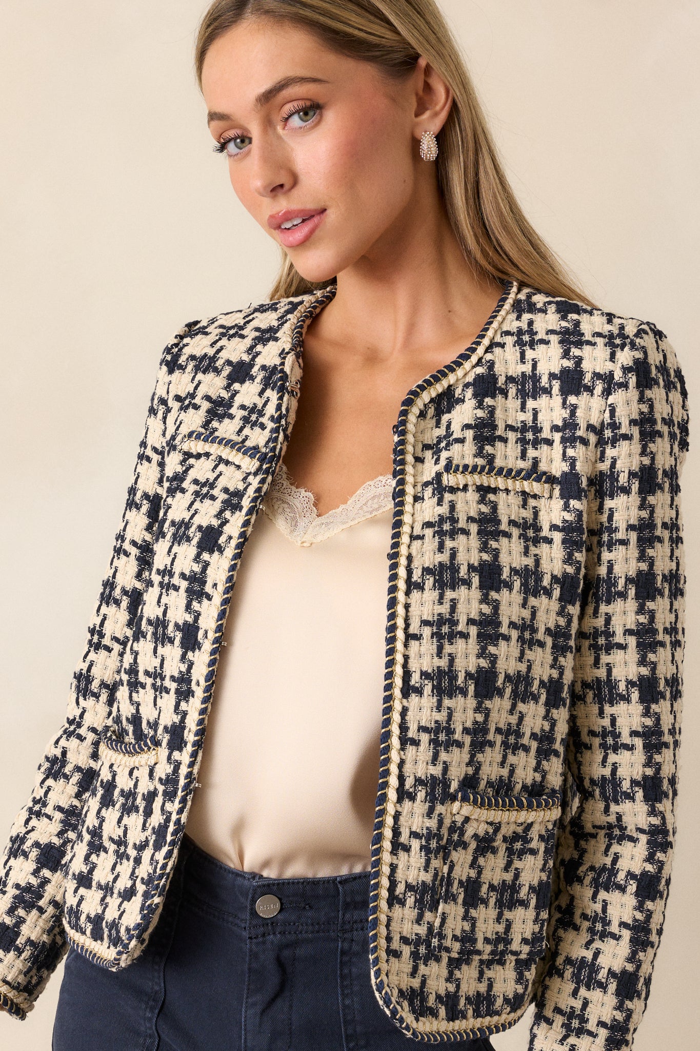 A full-length view of the navy tweed jacket featuring a houndstooth design, boxy fit, and gold rope twist detailing along the front and edges. The jacket is paired with functional front pockets.