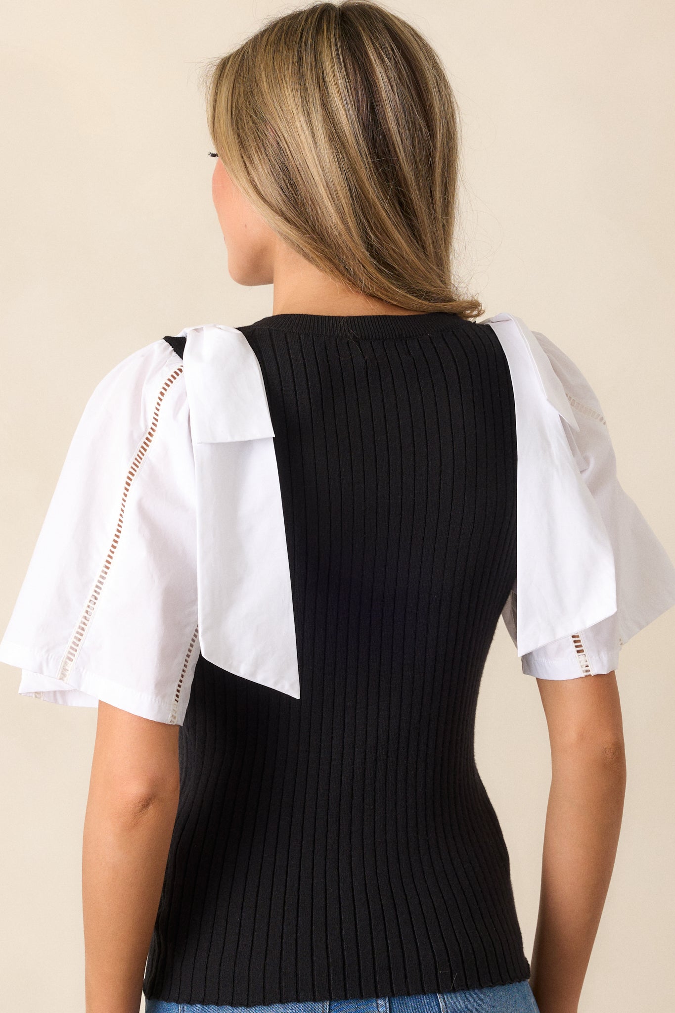 A rear view of the sweater top showing the color-blocked sleeves and ribbed texture on the back, with the shoulder bowties providing a charming finishing touch.