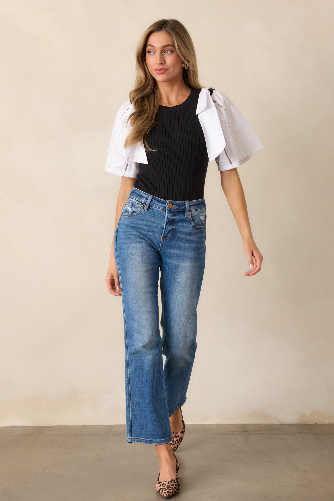 A front view of the black and white sweater top showcasing the round neckline and ribbed bodice, with the color-blocked sleeves featuring bowties on each shoulder.