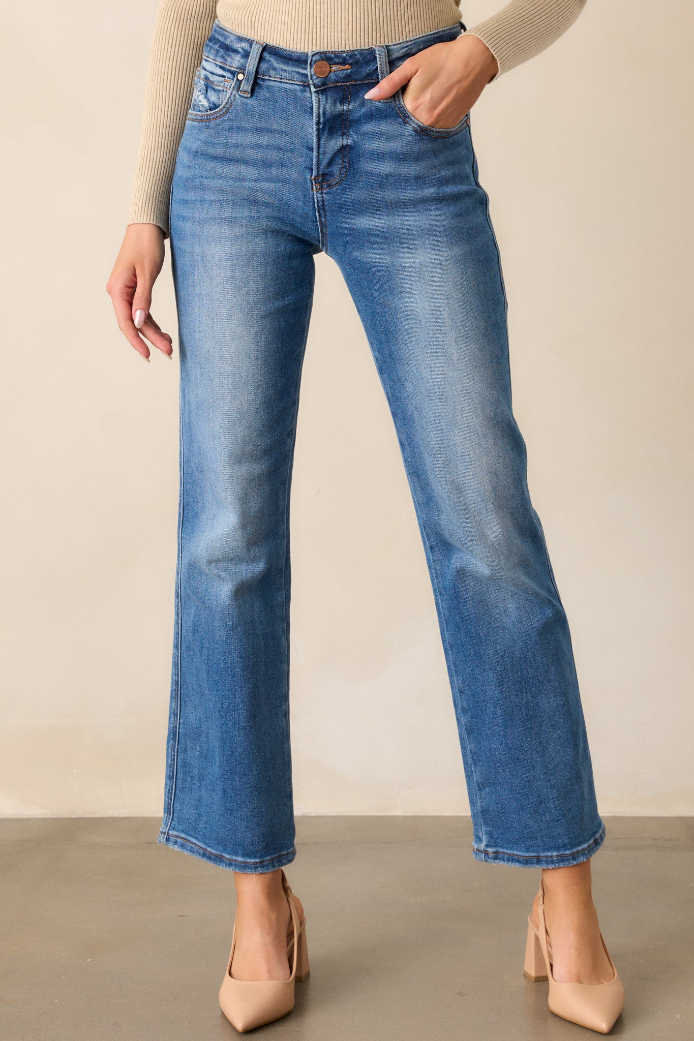 Front view of medium wash jeans featuring a high-rise design, functional front and back pockets, a button and zipper closure, a slightly distressed finish, and a straight leg cut.