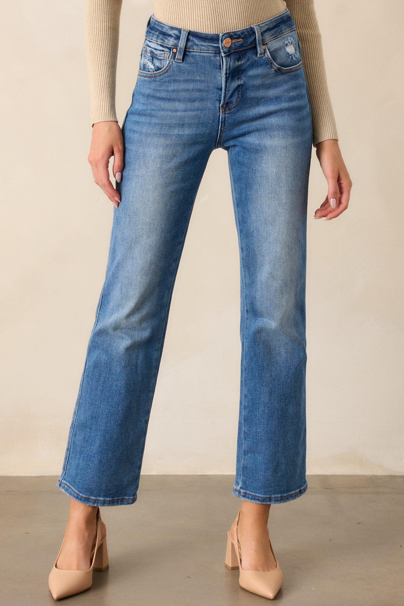 Straight leg medium wash jeans with functional pockets and a functional zipper, with slight distressing around the pockets and a high rise fit. 