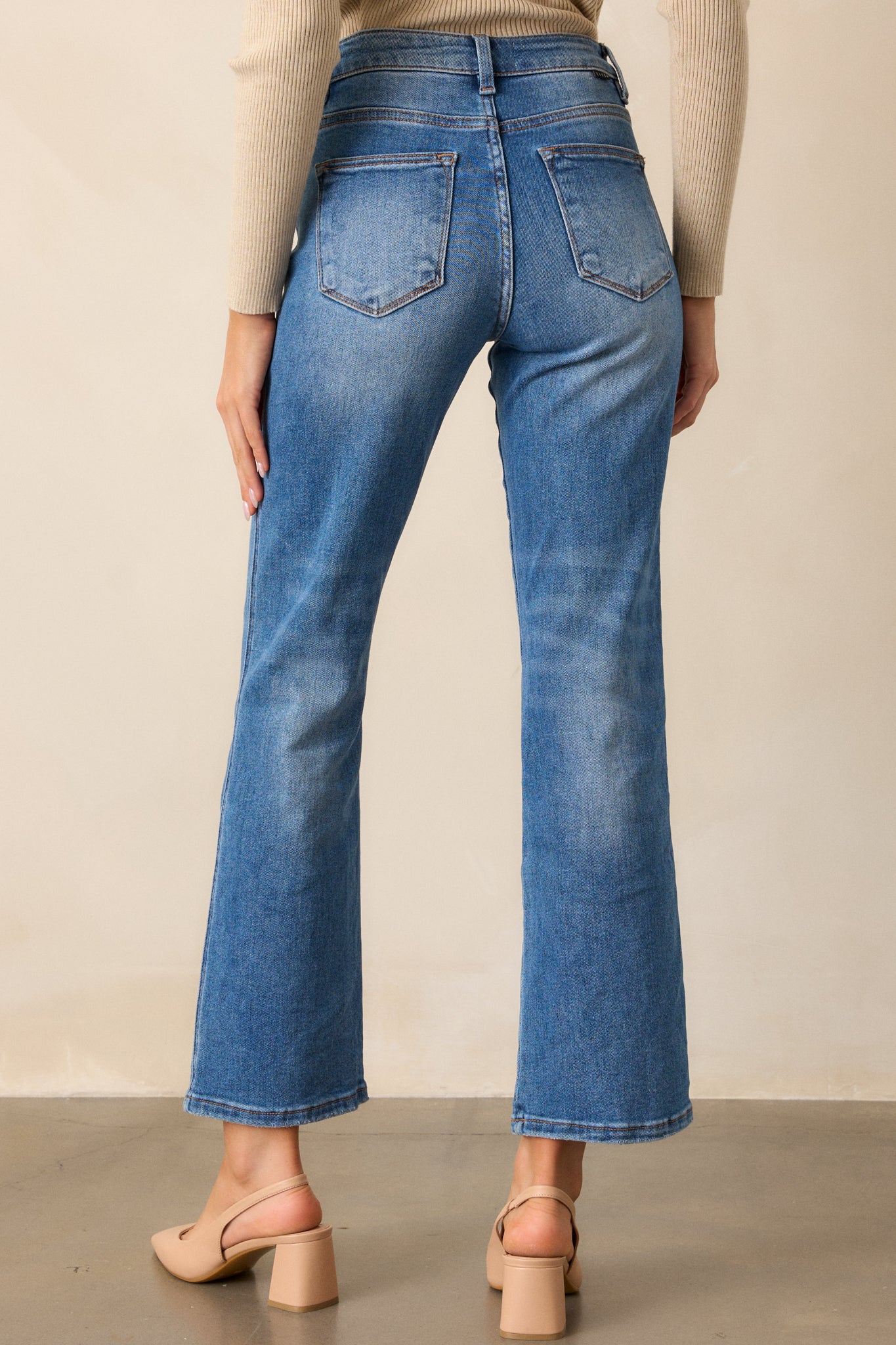 Back view of medium wash jeans featuring a high-rise design, functional front and back pockets, a button and zipper closure, a slightly distressed finish, and a straight leg cut.