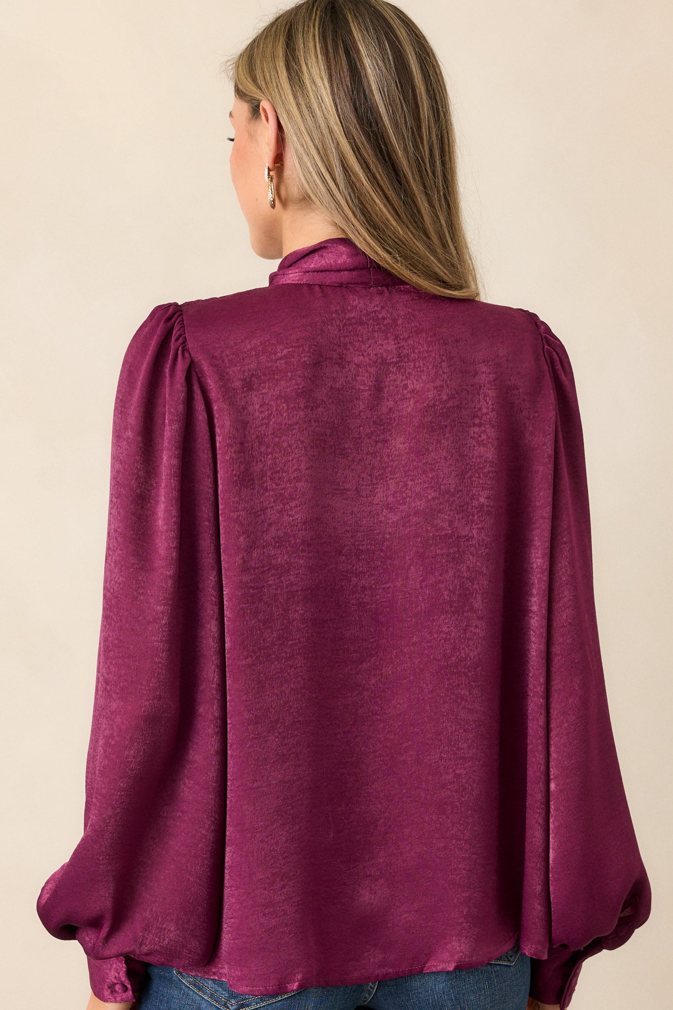 Back view of a dark purple top highlighting the high neckline with self tie and the flowy balloon sleeves.