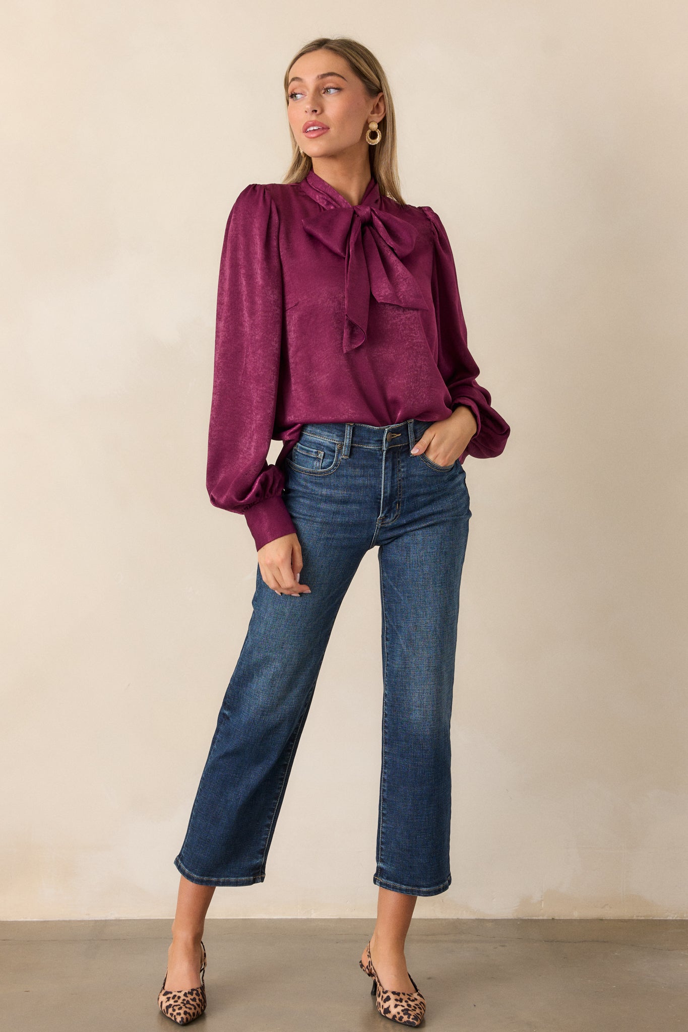 Full length view of a dark purple top with a high neckline, adjustable self tie, flowy balloon sleeves with two buttons at the cuff, and a relaxed fit.