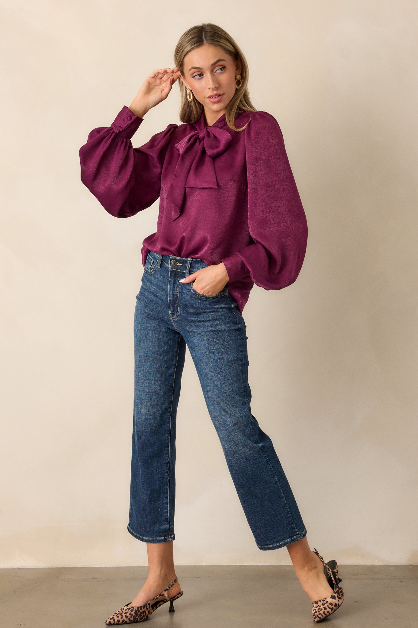 Full length view of a dark purple top showcasing the high neckline with adjustable self tie, flowy balloon sleeves with buttoned cuffs, and relaxed fit.