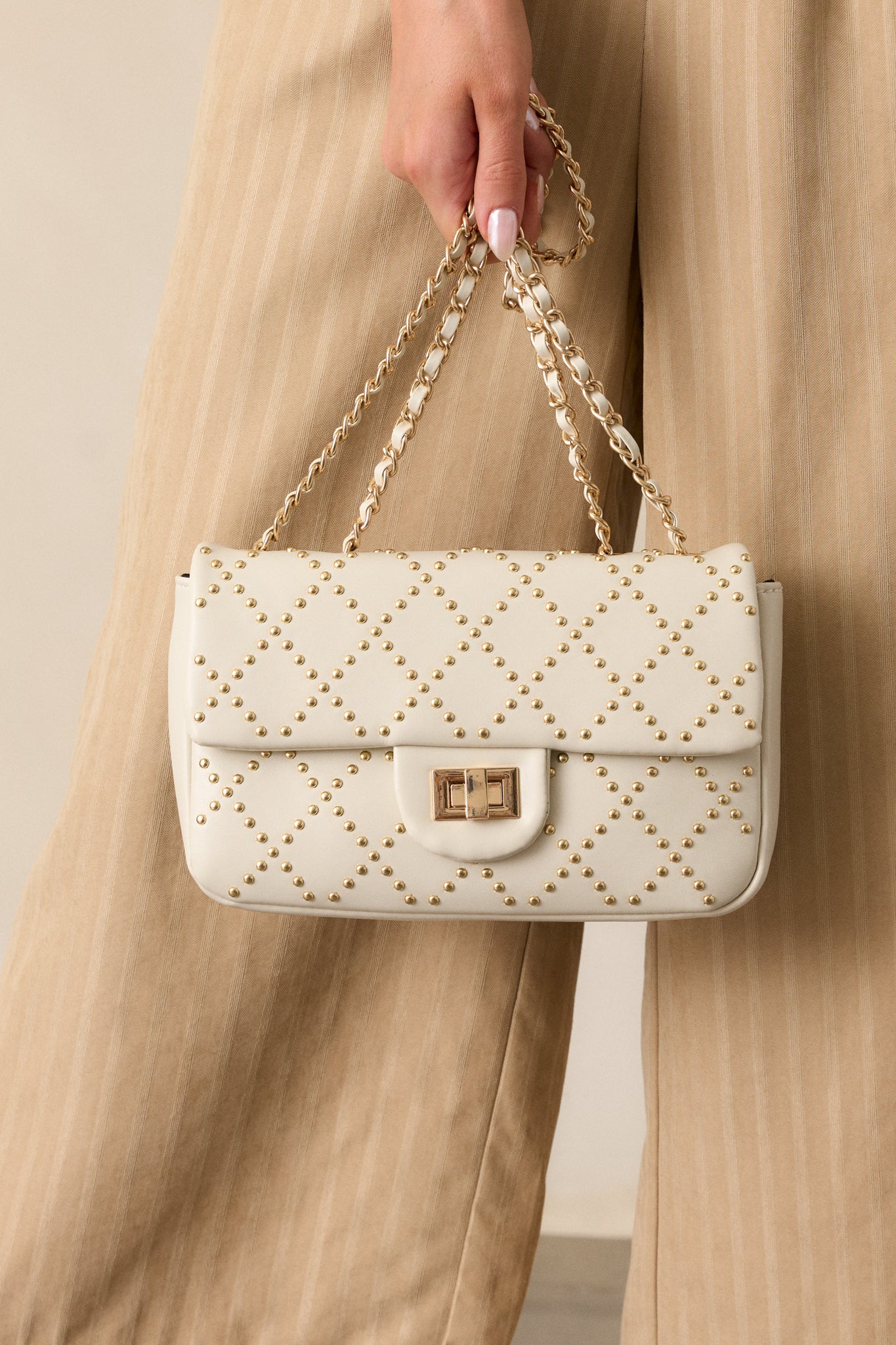 Close-up on the braided ivory and gold chain handles, emphasizing the texture and design of the chain against the studded quilted body.