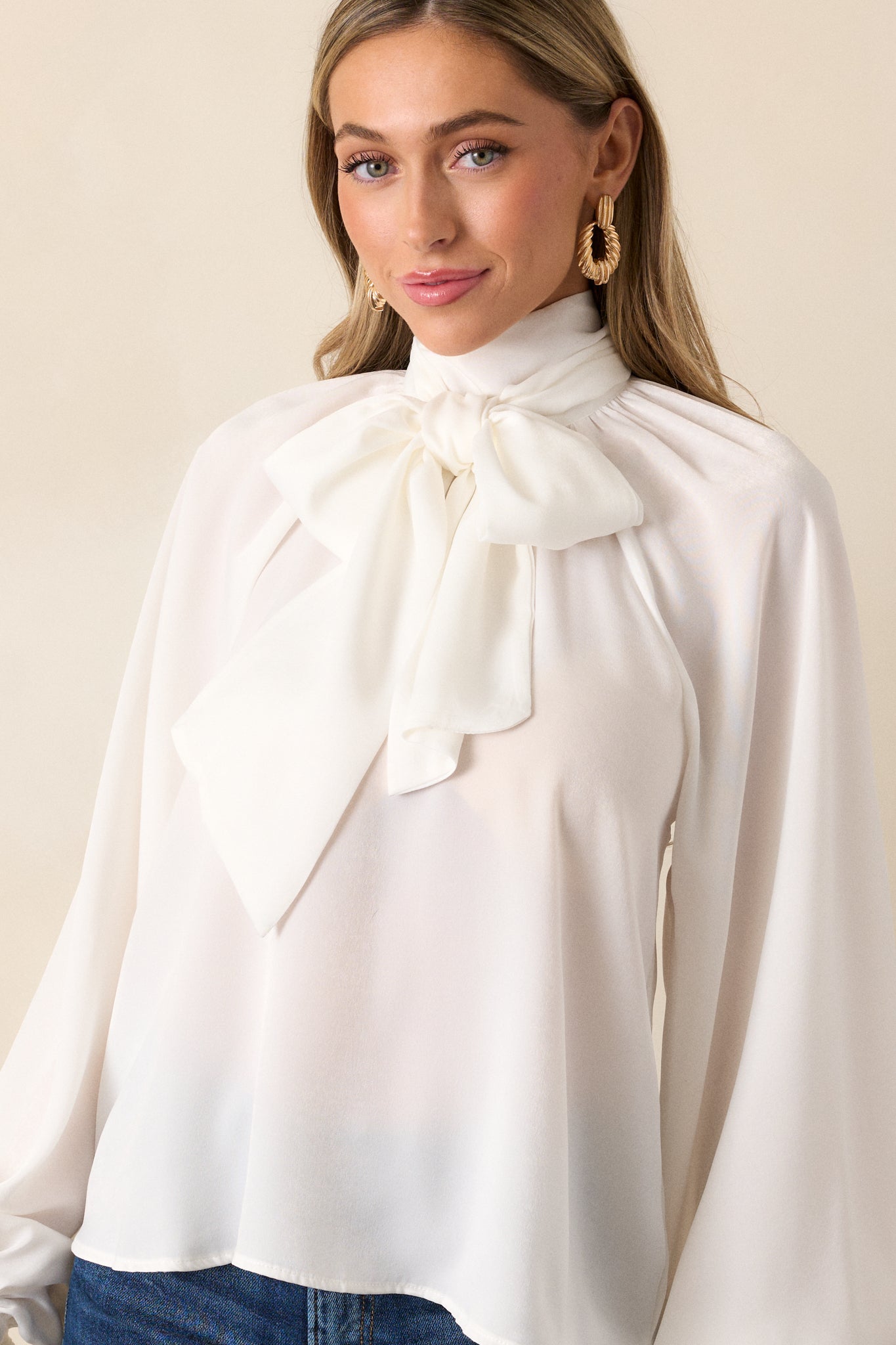 A front shot of the top featuring a high neckline, balloon sleeves with buttoned cuffs, and a flowy fit. The adjustable self-tie around the neck adds a touch of detail to the relaxed silhouette.