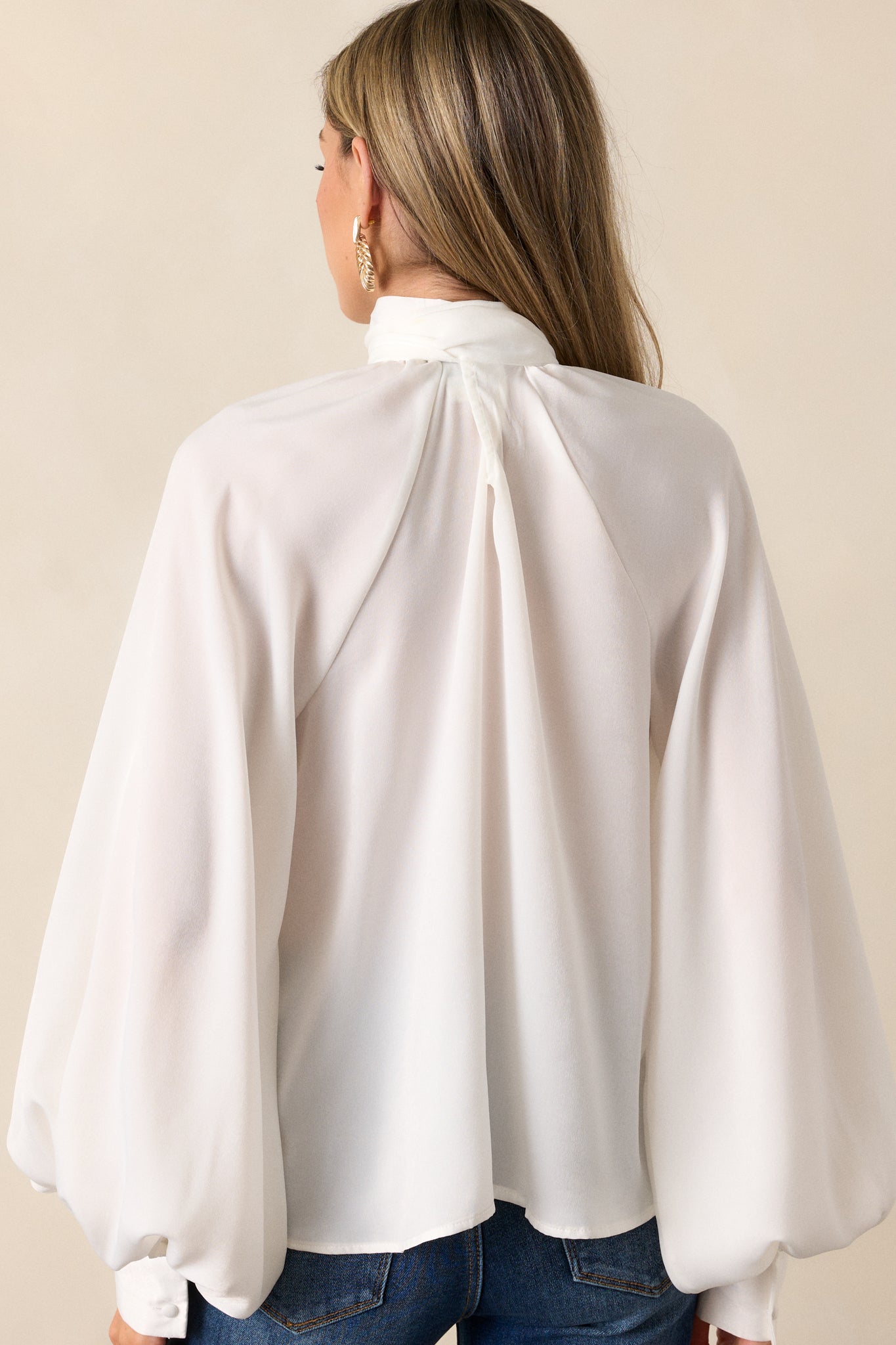 A back view of the top showing the flowy fit, with emphasis on the balloon sleeves and their buttoned cuffs. The high neckline and self-tie detail at the back of the neck are also visible.