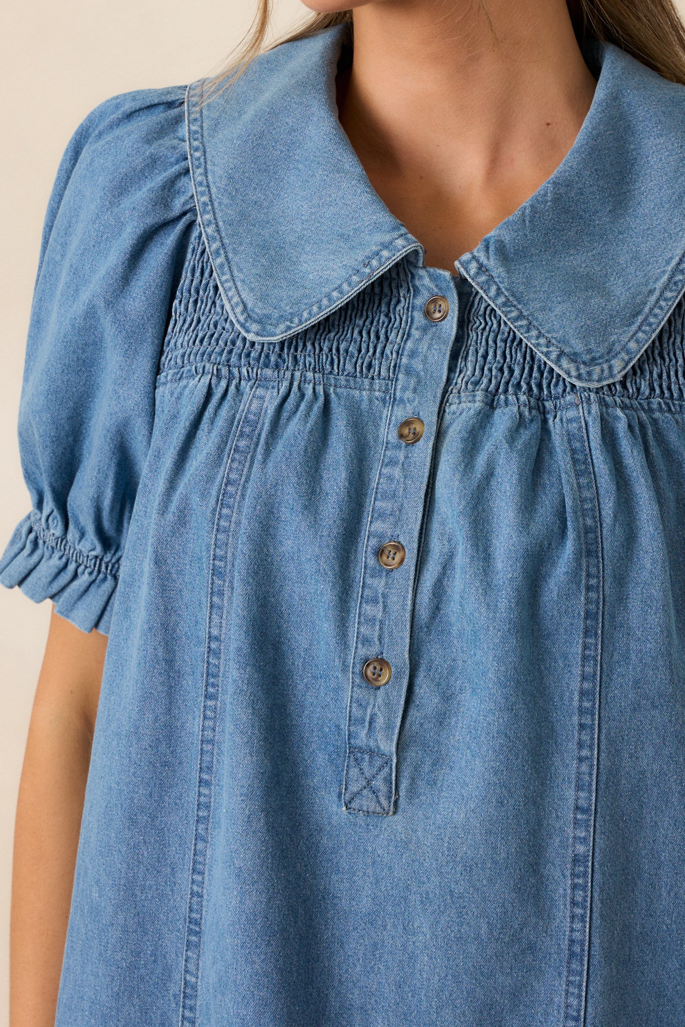 Close-up of the functional buttons down the front of the medium wash denim dress, showcasing the delicate stitching and collar design.