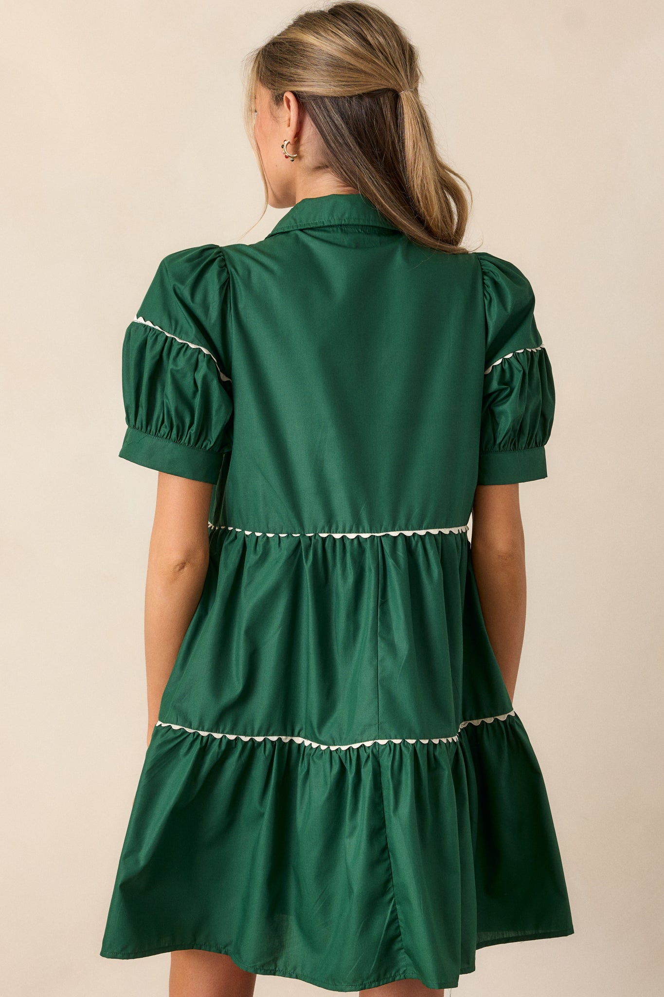 Back view of the emerald mini dress, displaying the tiered design, white scalloped hem, and the shape of the puff sleeves from behind.