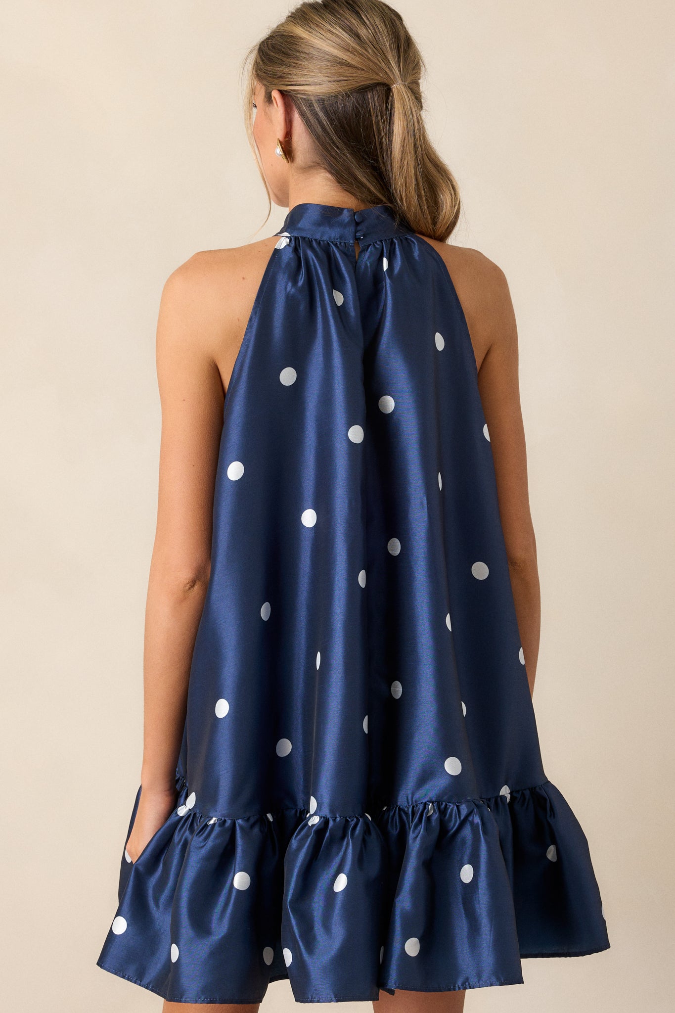 A back view of the dress, focusing on the halter neckline with button clasps and the overall flow of the fabric. The ruffle bottom hem and mini length are visible from this angle.