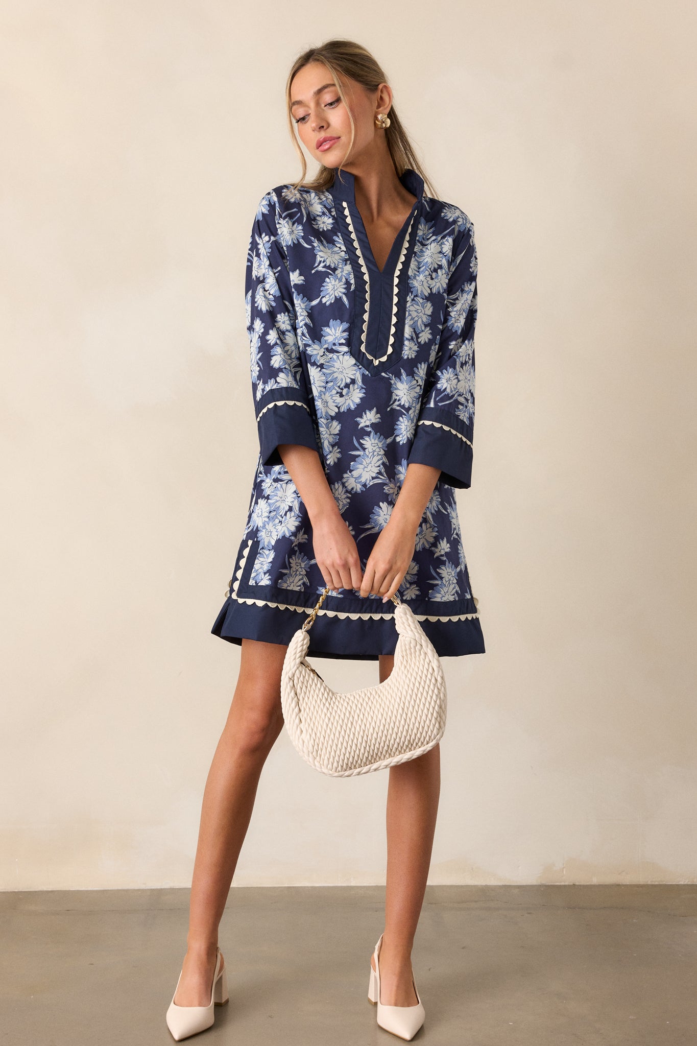 Full view of the navy dress, featuring a v-neckline with white scalloped trim, long sleeves with wide cuffs, and a floral pattern in white and light blue.