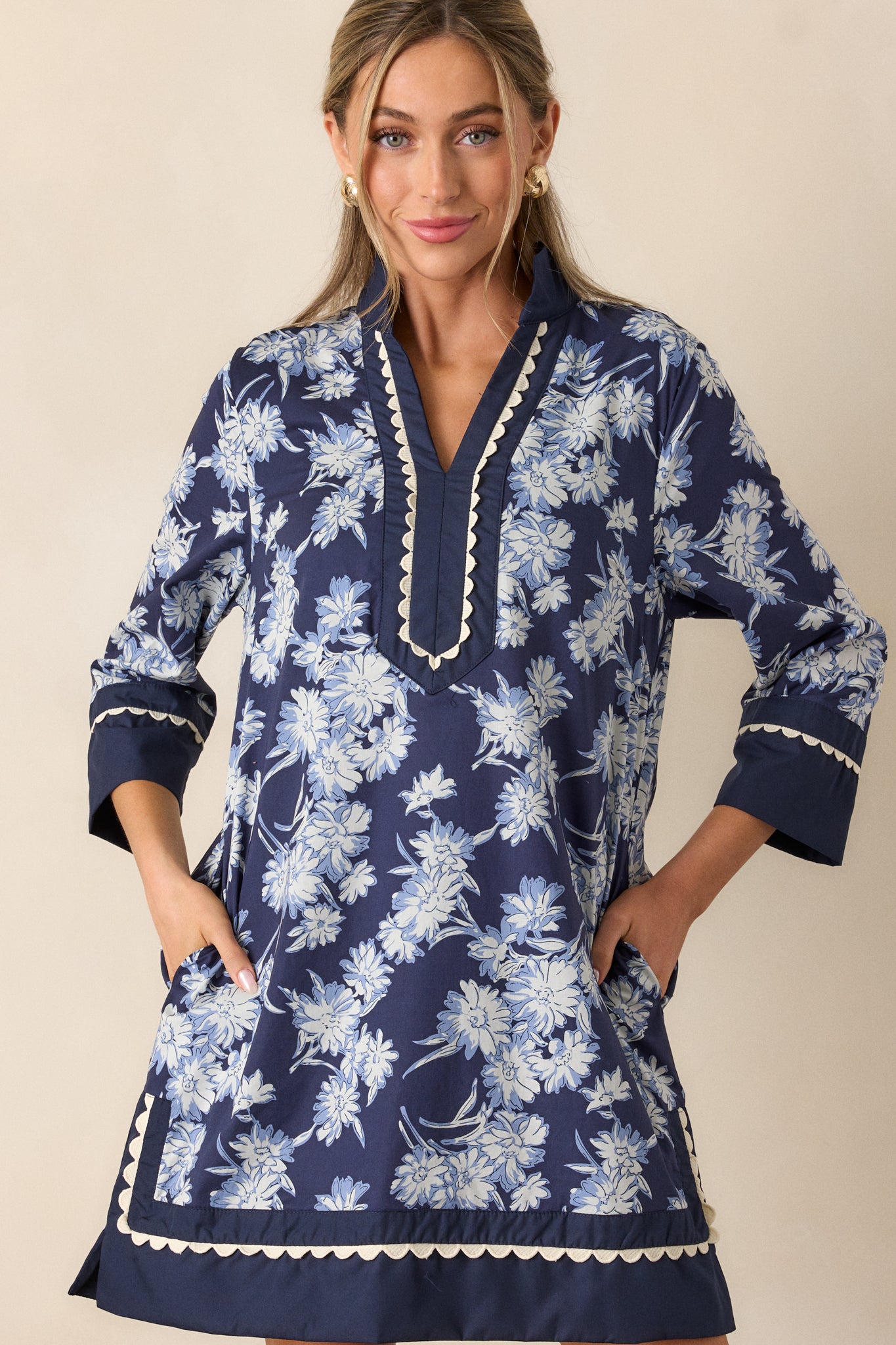 Front view of the navy mini dress, emphasizing the white and light blue floral pattern, v-neckline with scalloped trim, and long sleeves with wide cuffs.