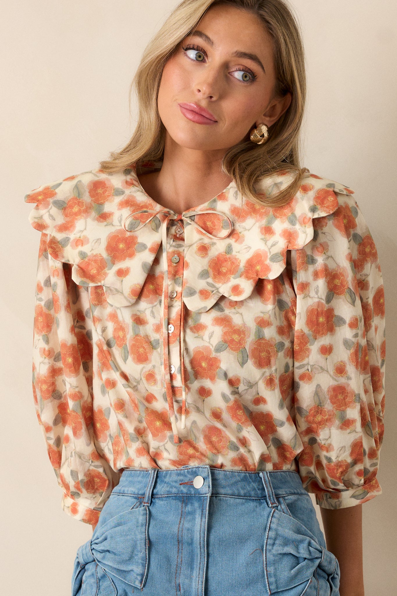 Close-up of the apricot blouse’s peter pan collar with a self-tie detail, showing part of the floral pattern around the neckline.