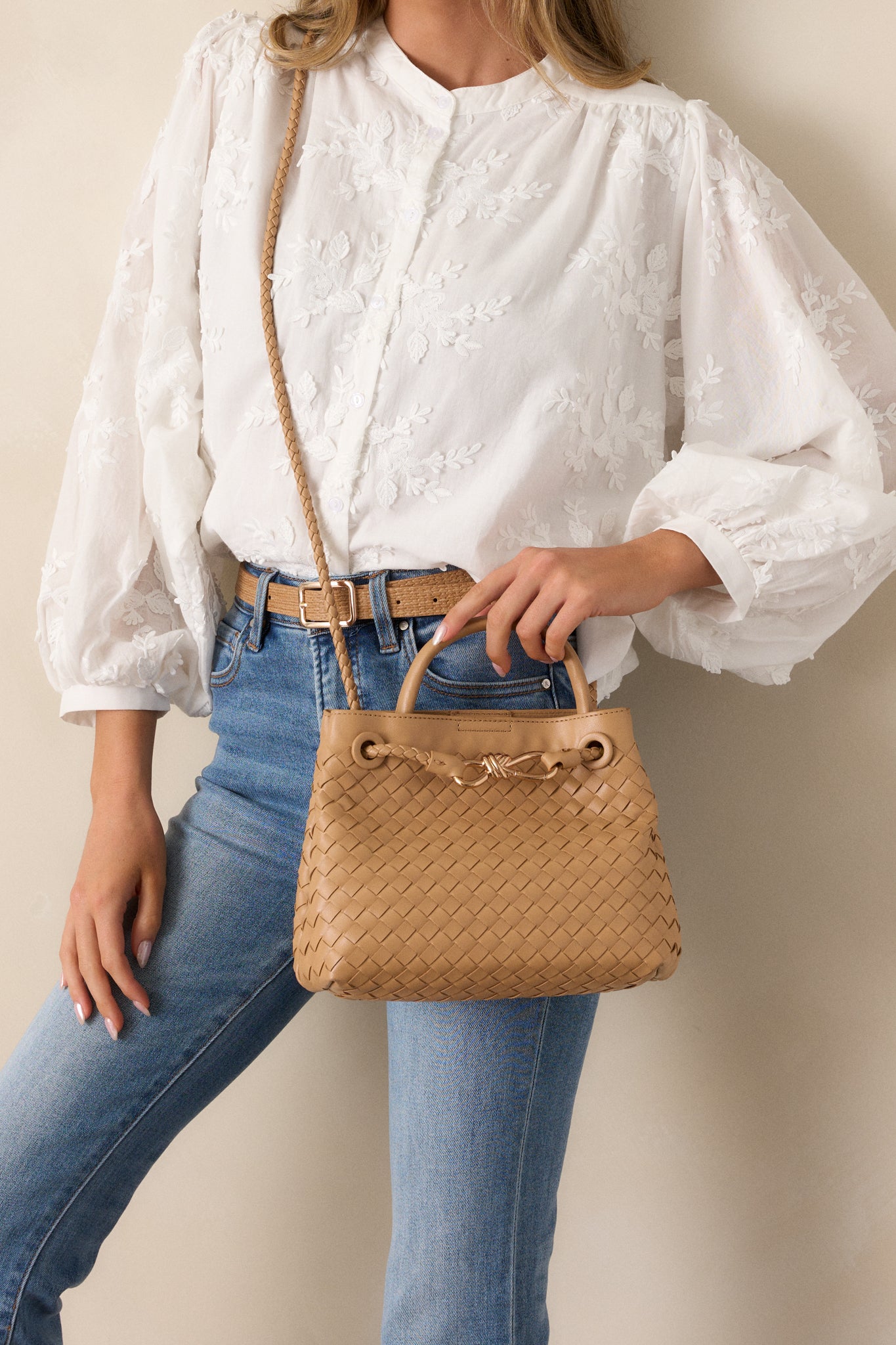 A full view of the tan faux leather handbag with its short handle shown prominently for handbag use and the woven shoulder strap hanging down.