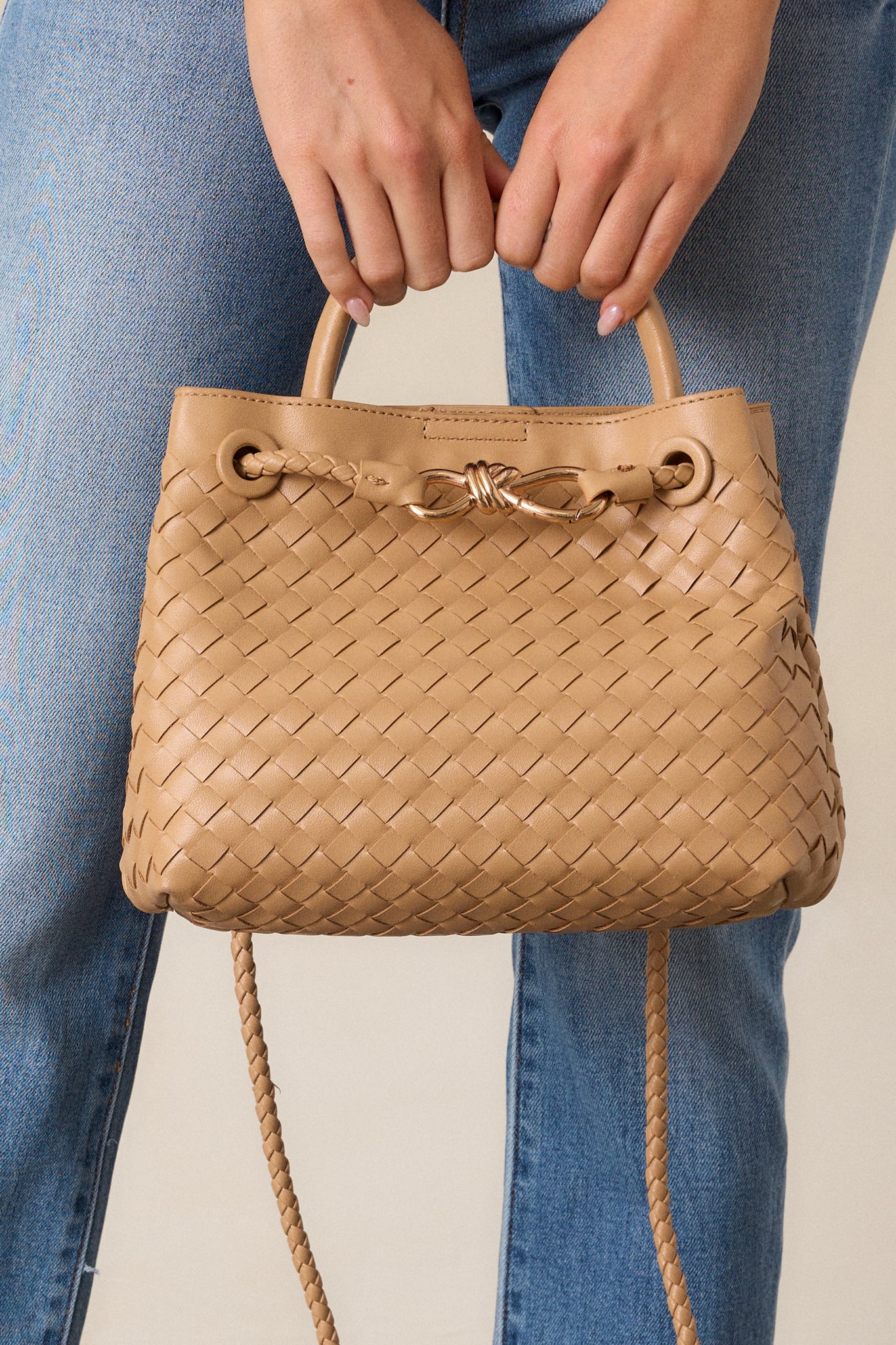 A close-up of the top section, highlighting the short handle, woven strap attachment, and the tan faux leather texture.