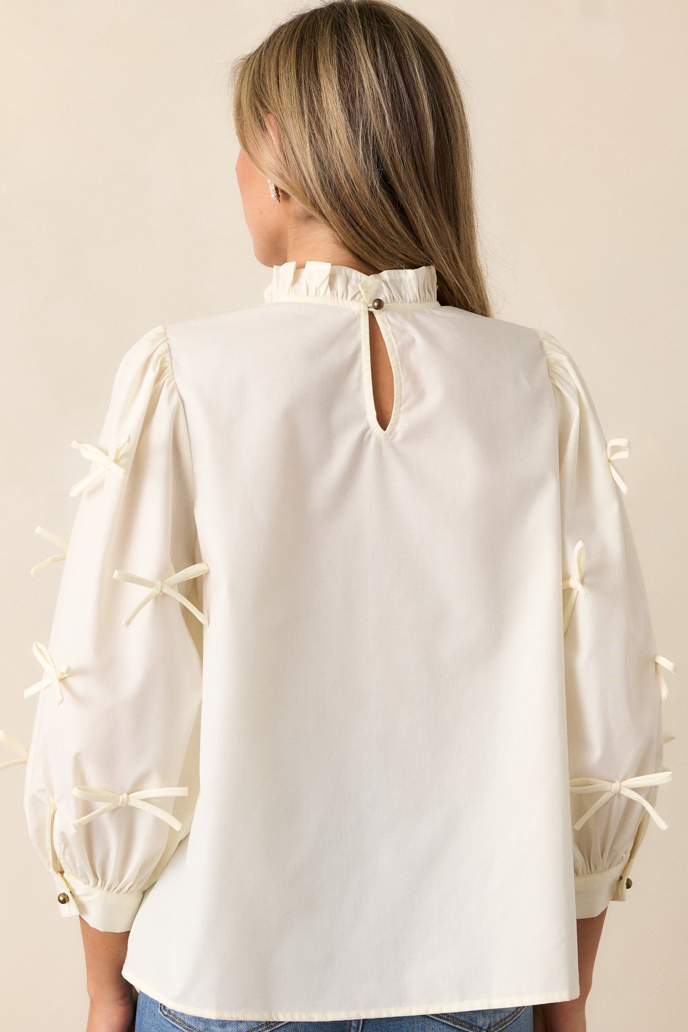 Back view of the ivory blouse, featuring a high ruffle neck with a keyhole and button closure, showing the relaxed fit and 3/4 sleeves.