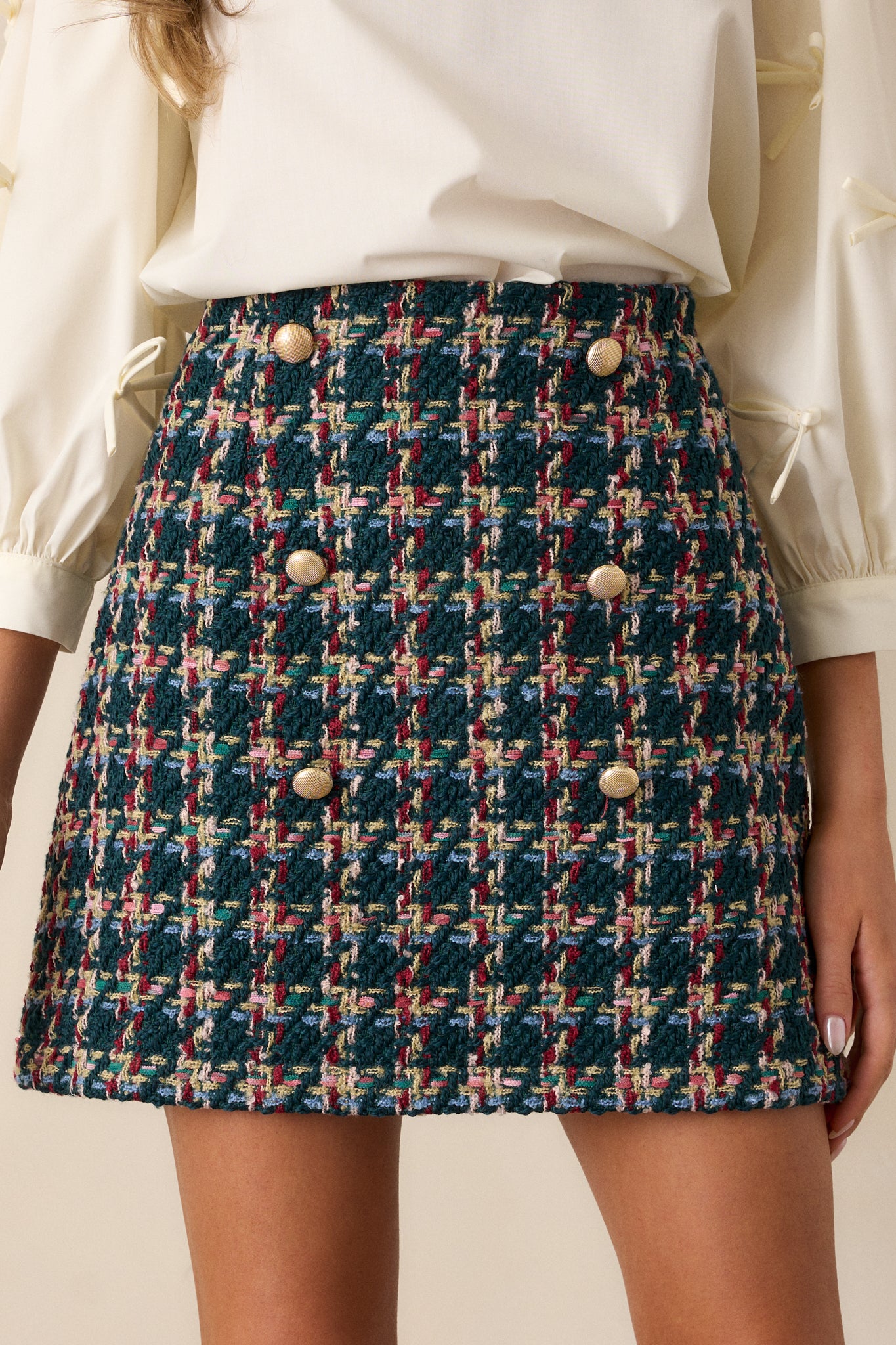 Close-up of the gold embellished buttons against the tweed fabric on the emerald mini skirt, showing the intricate button details.