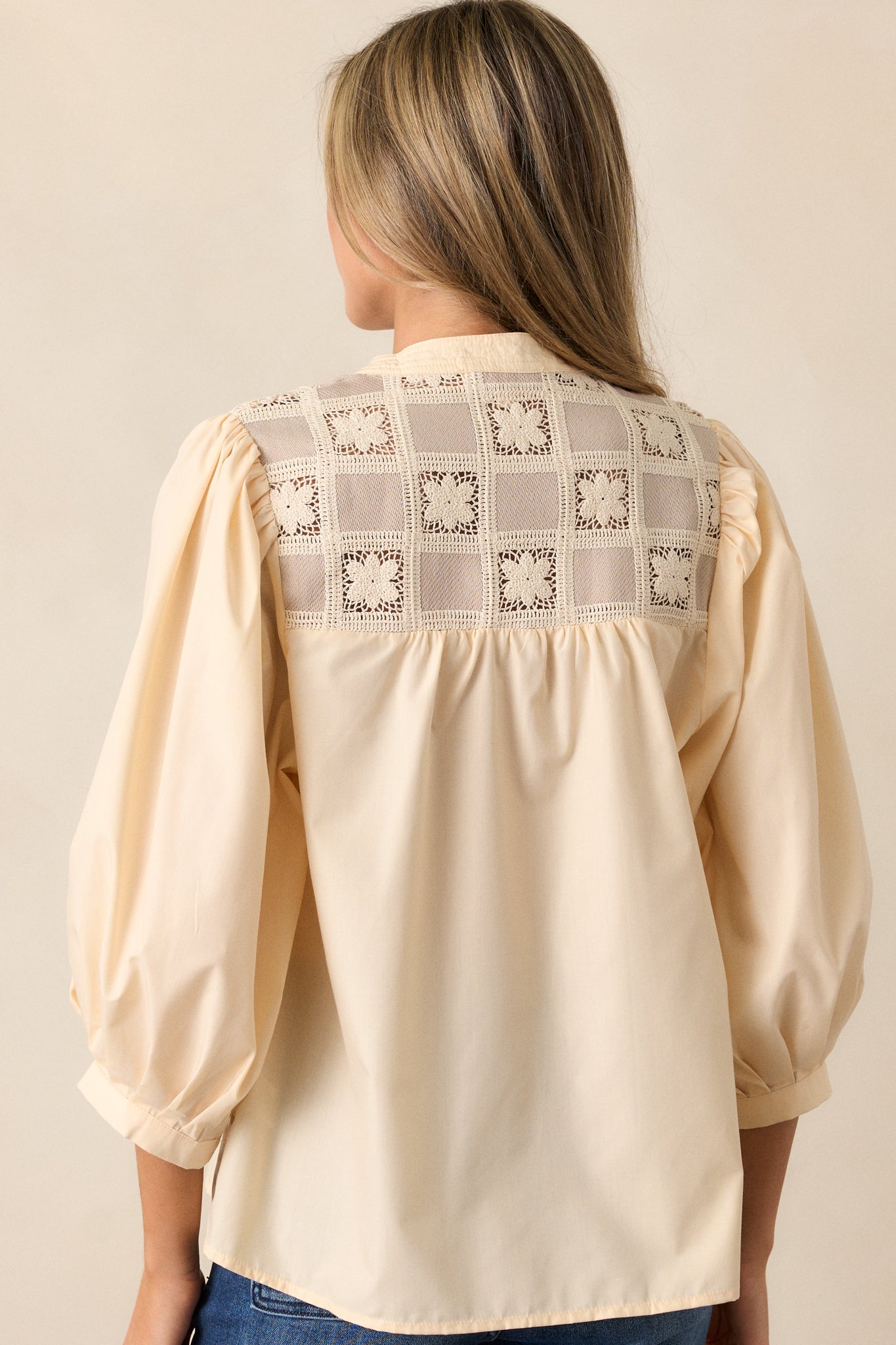 Back view of the almond blouse with a relaxed fit, showcasing the checkered floral stitching across the back and puff sleeves.