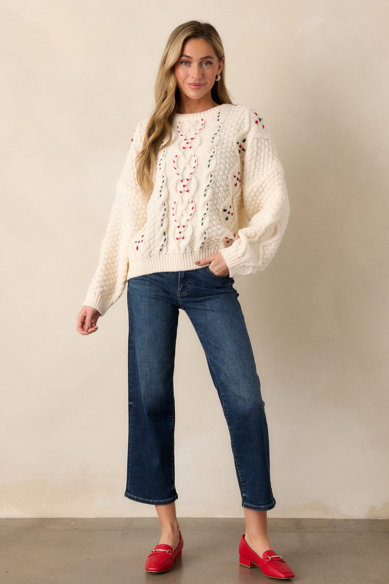 Oversized ivory sweater with a mix of cable knit patterns, ribbed hems, and subtle red and green thread details on the round neckline and sleeves.