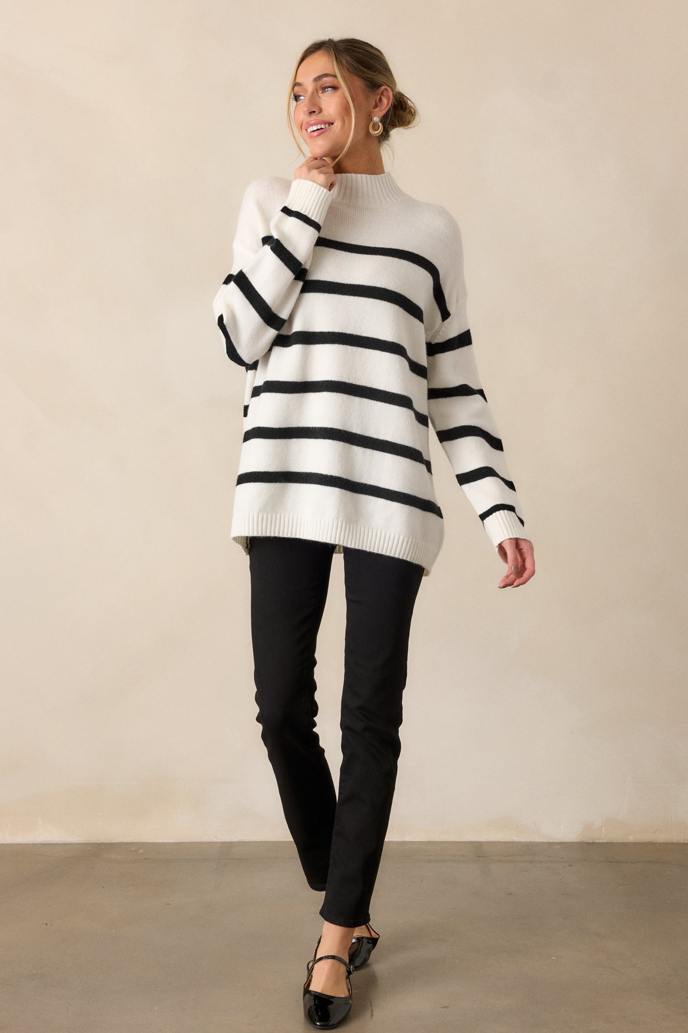 Front view of the white sweater with black horizontal stripes, highlighting its oversized fit and high mock neckline.