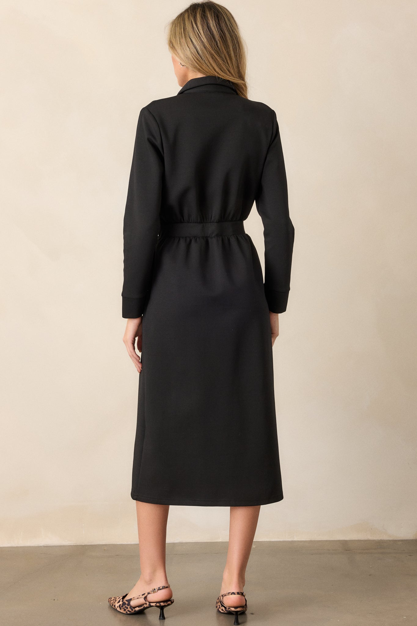 Back view of the black dress, displaying the smooth lines of the fabric and the elegance of the midi length from behind, along with the long sleeves.





