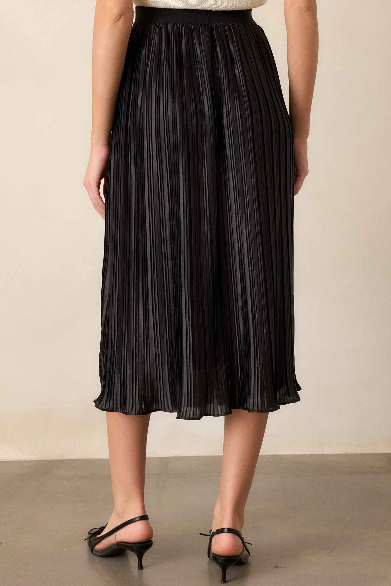 Back view of the black skirt, displaying the high-waisted design and the smooth transition of the pleated fabric from behind.