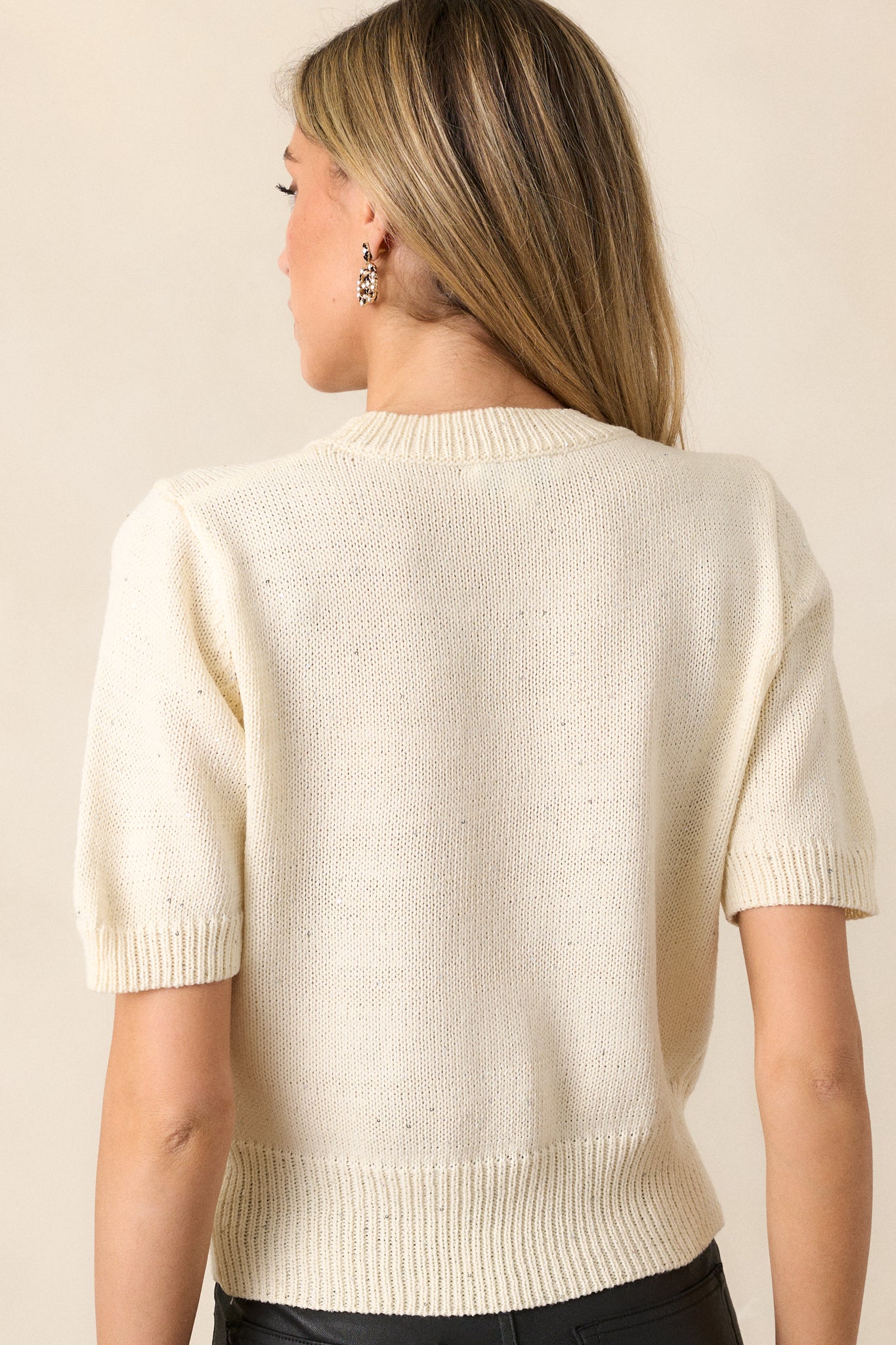 View of the back of the top, featuring the continuous knit design, sequins, and the wide rib knit bottom hem for a polished finish.