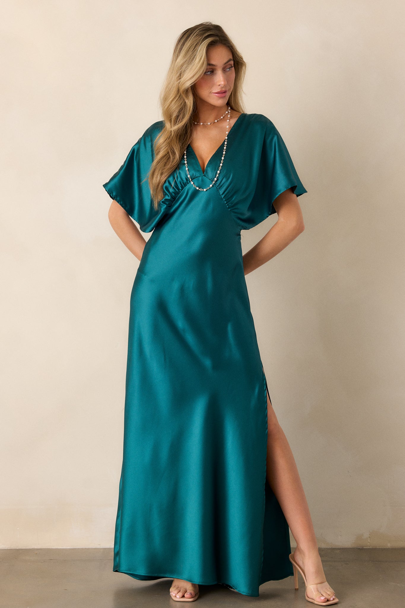 A full view of the teal dress, showcasing its deep V-neckline, side slit, and glossy satin finish.