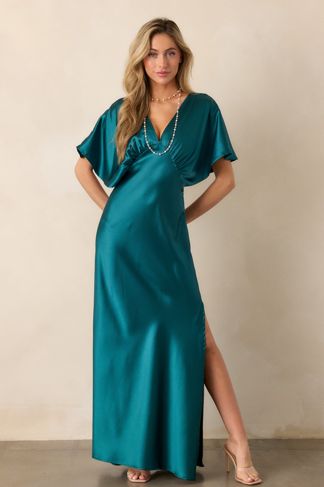 Front view of a teal dress with a shiny satin fabric, showing the deep V-neckline and relaxed kimono sleeves.