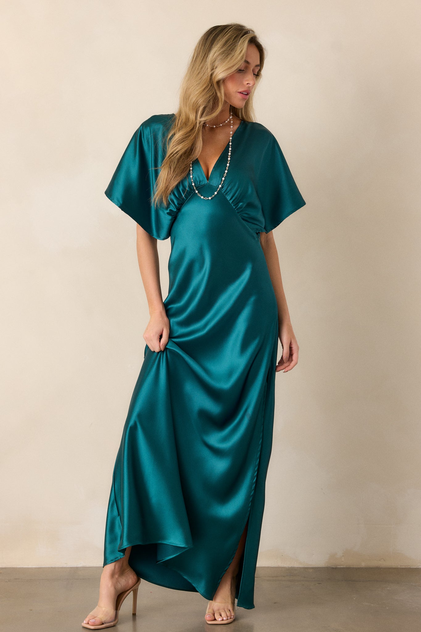 Full-length image focusing on the fit of the teal satin dress, with a side slit and kimono-style sleeve draping.