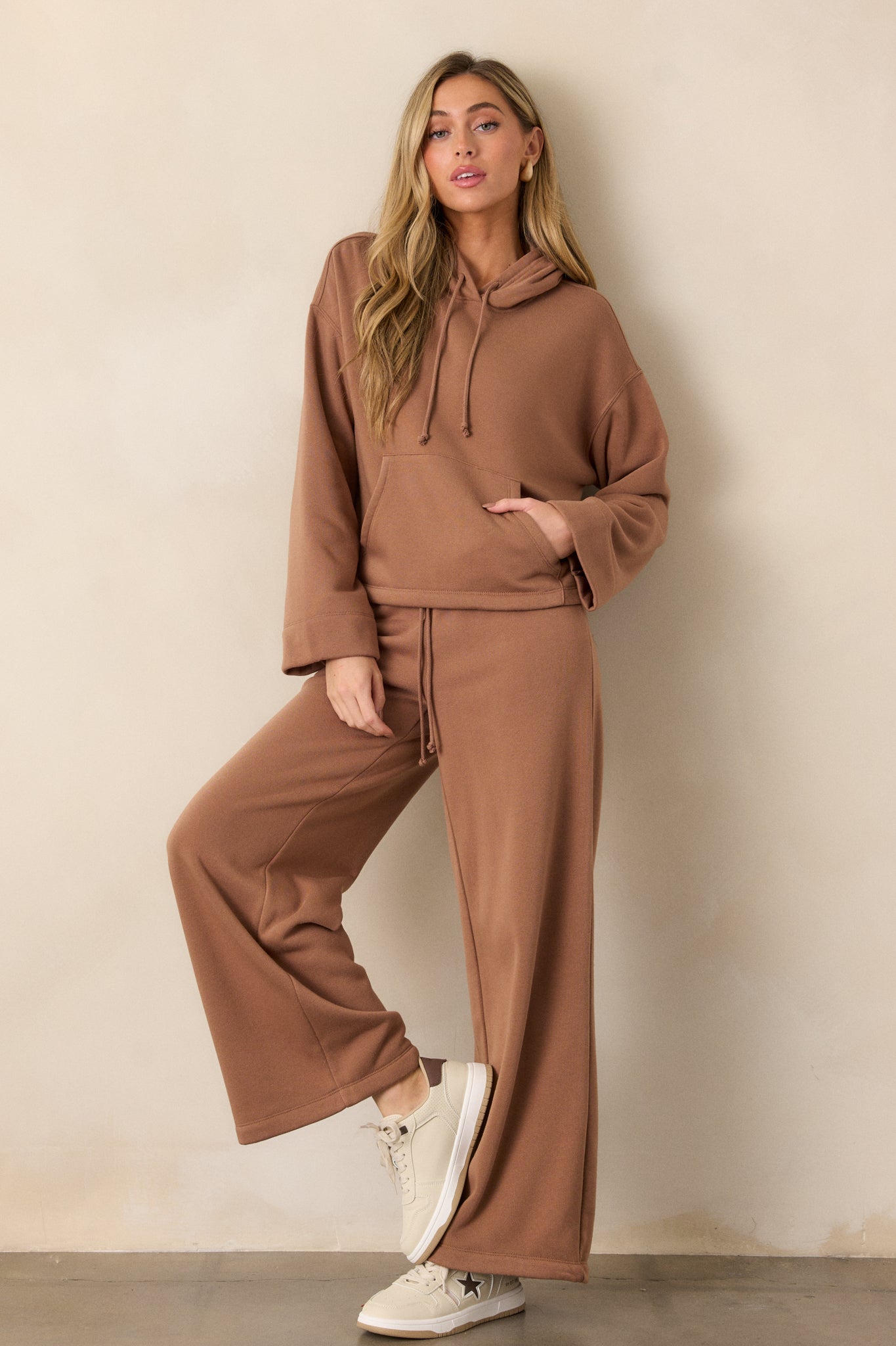 Full body image of the brown sweatshirt, highlighting the loose long sleeves, hooded neckline, and roomy kangaroo pocket.